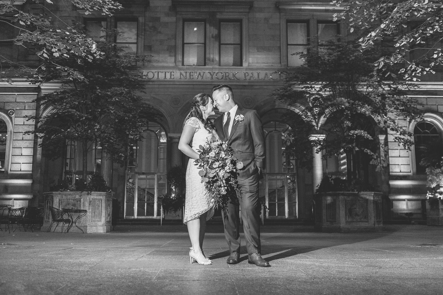 Couple shares a kiss in black and white photo outside a grand historic building at night.
