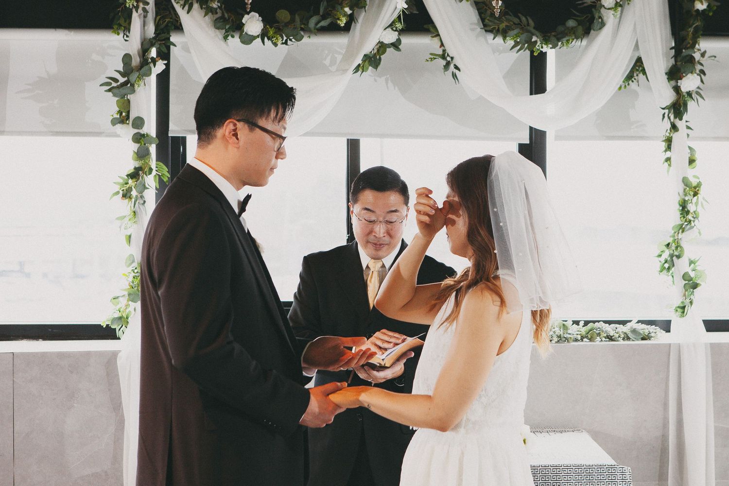 Groom places wedding ring on brides finger during intimate ceremony with floral arch backdrop.