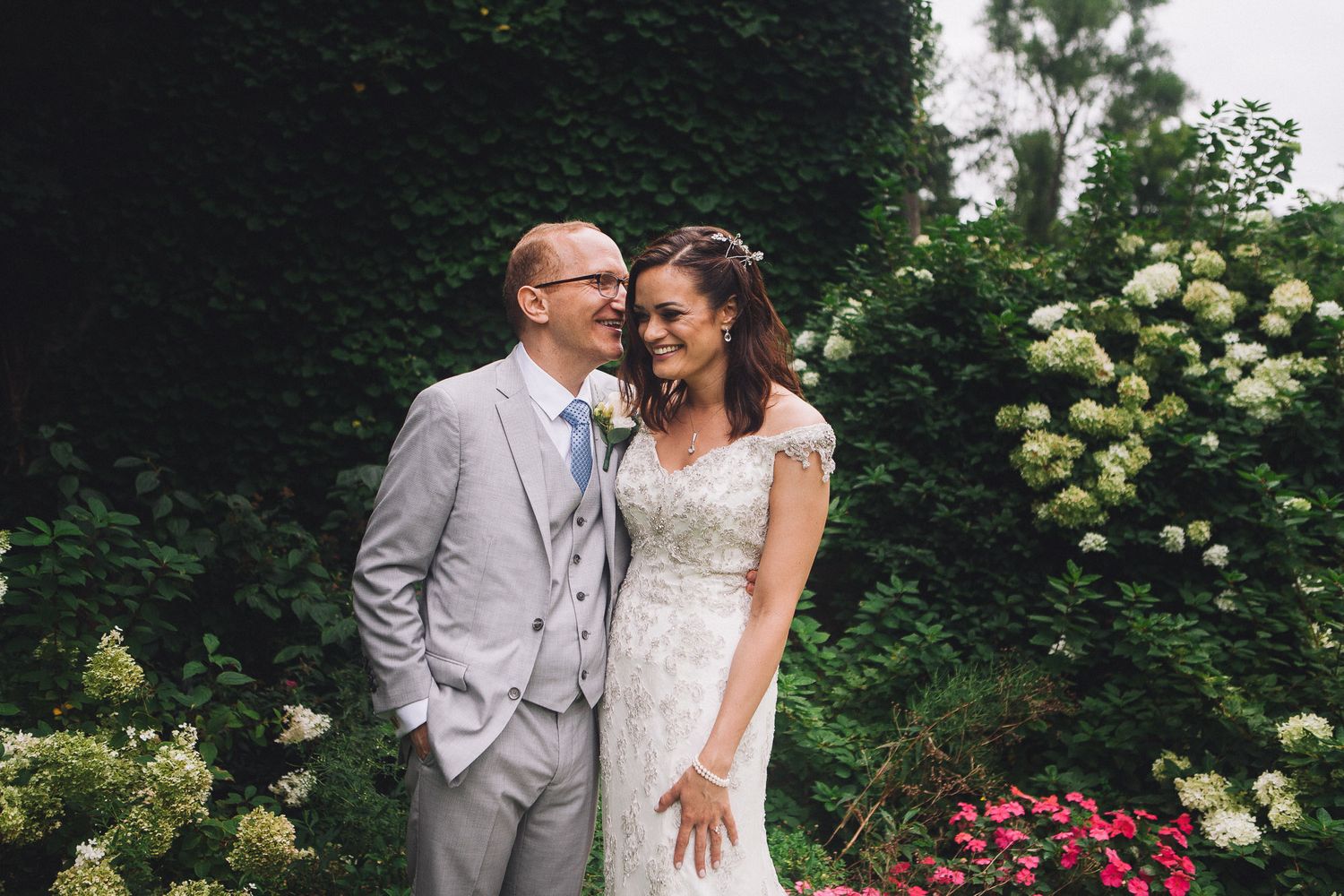 Bride and groom laughing together near white hydrangeas in romantic wedding portrait.