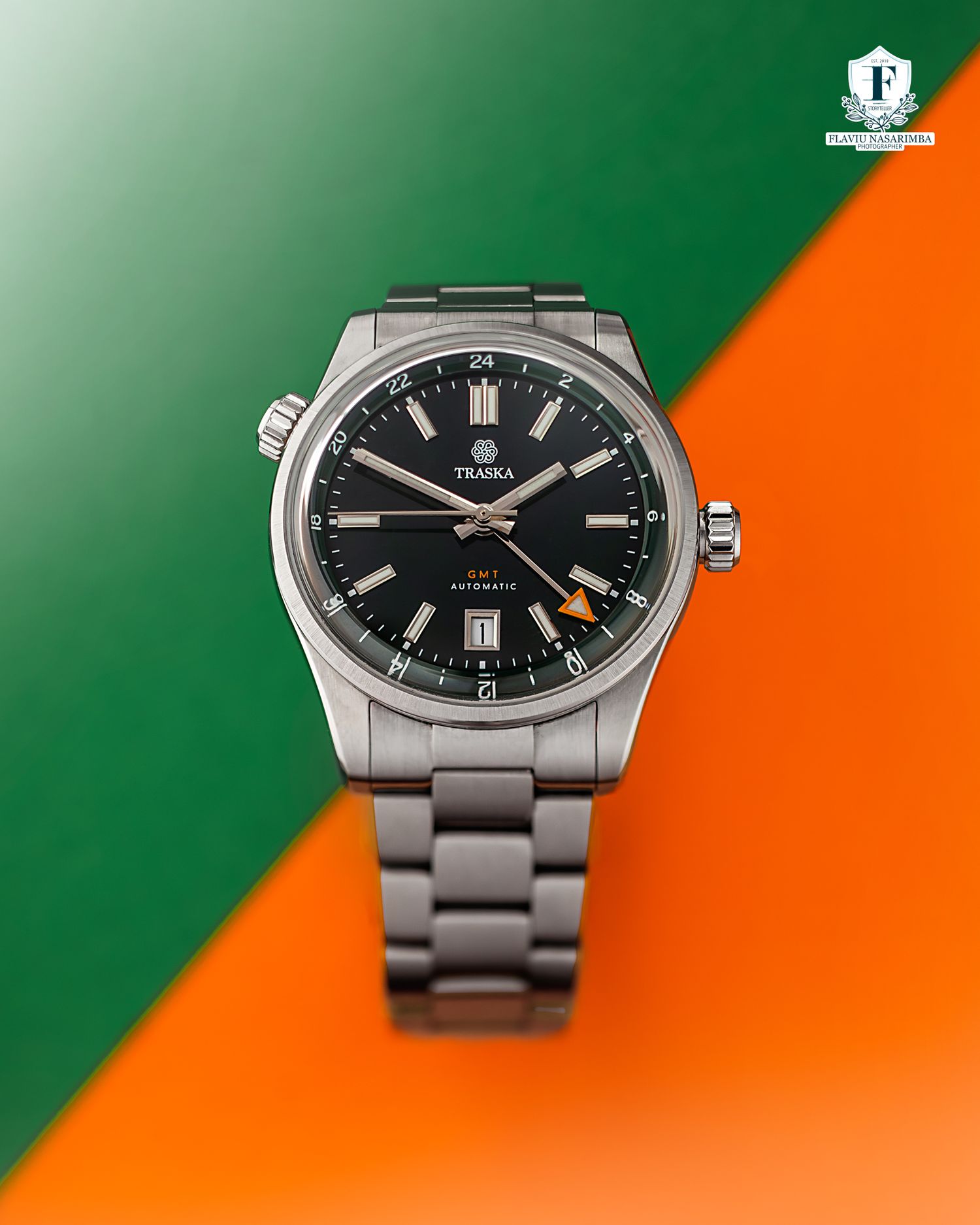 Traska GMT automatic stainless steel watch with black dial on green and orange background.
