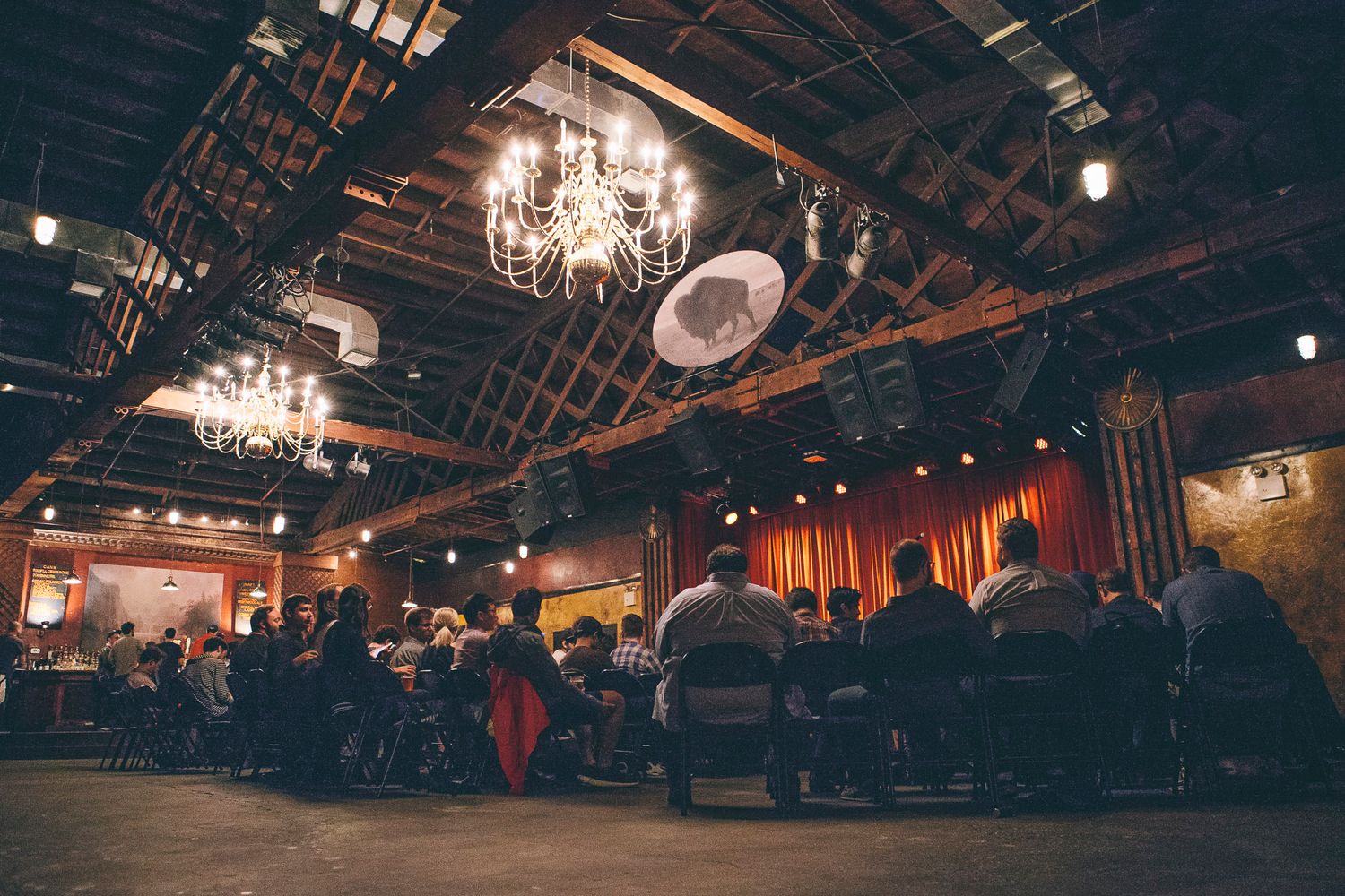 Guests seated at tables in a warmly lit rustic event space with exposed ceiling beams.