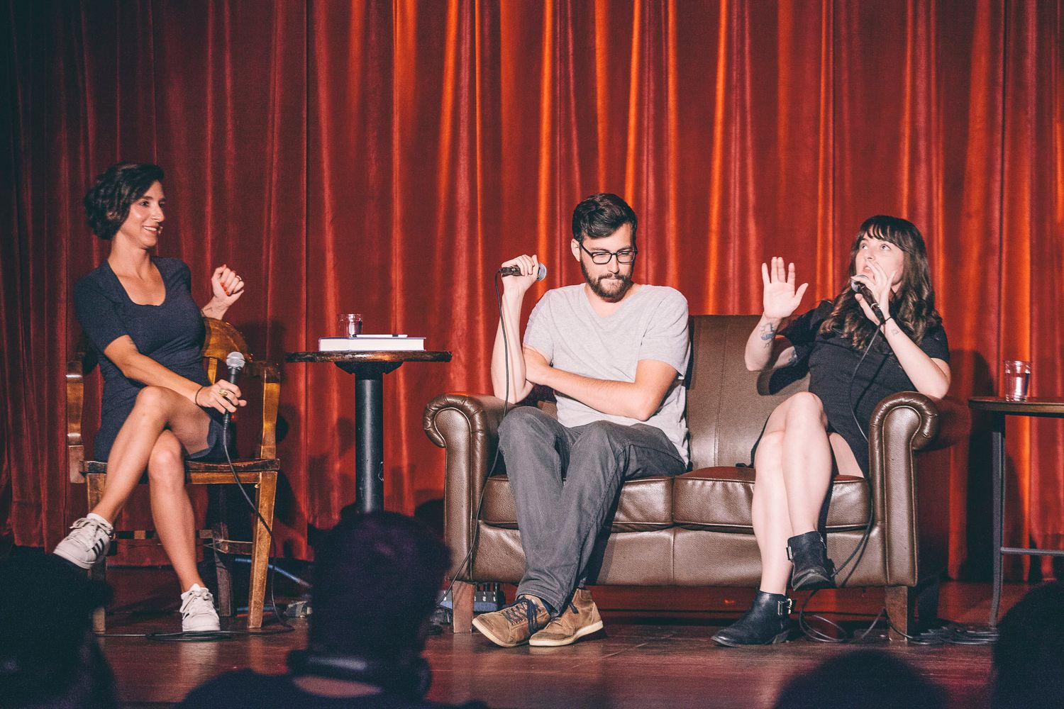 Three panelists engaged in animated discussion on stage with red curtain background.