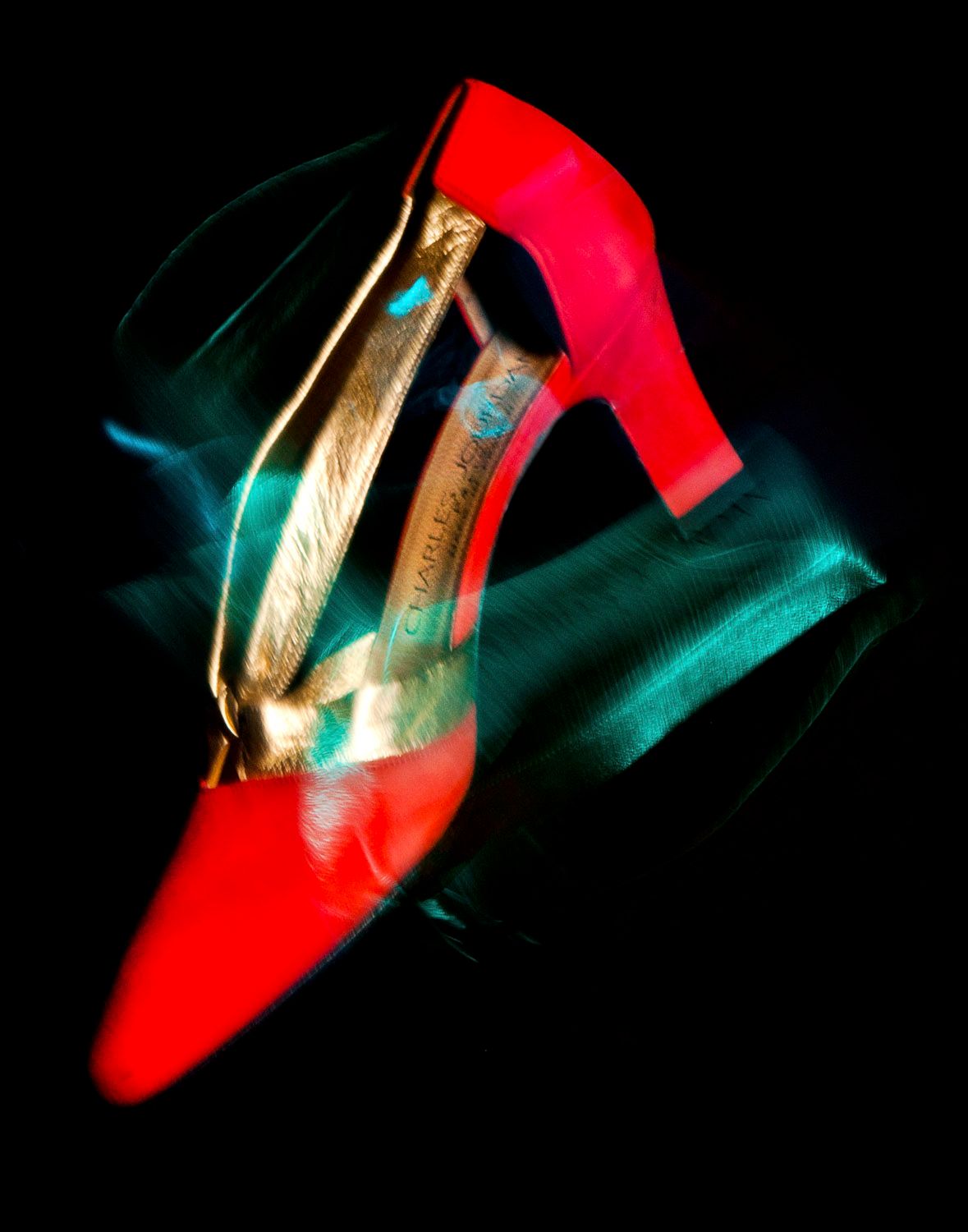 Artistic long exposure photograph of a red high heel shoe with motion blur on black background.