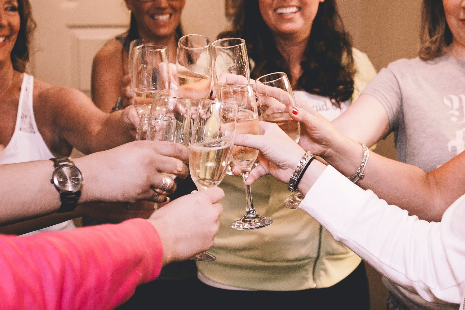 Group of women celebrating with champagne toast, clinking glasses together in joyful pre-wedding gathering.