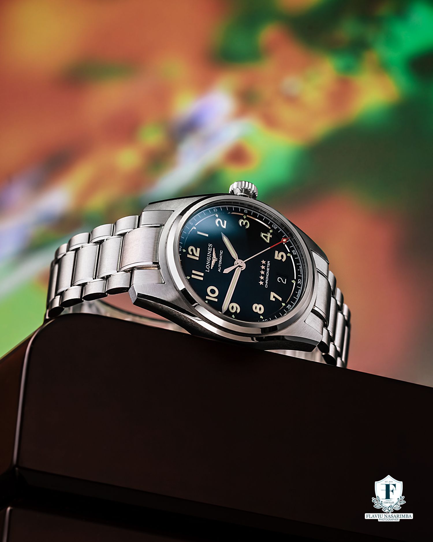 Longines Spirit stainless steel watch with deep blue dial on dark display box with colorful backdrop.
