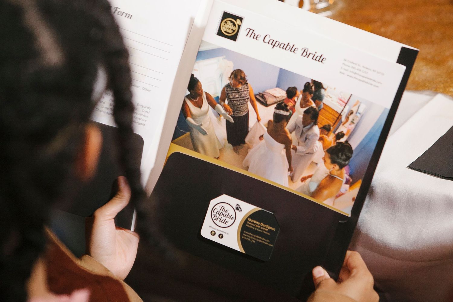 Close-up of hands holding The Capable Bride wedding planning brochure featuring a bridal party photo.