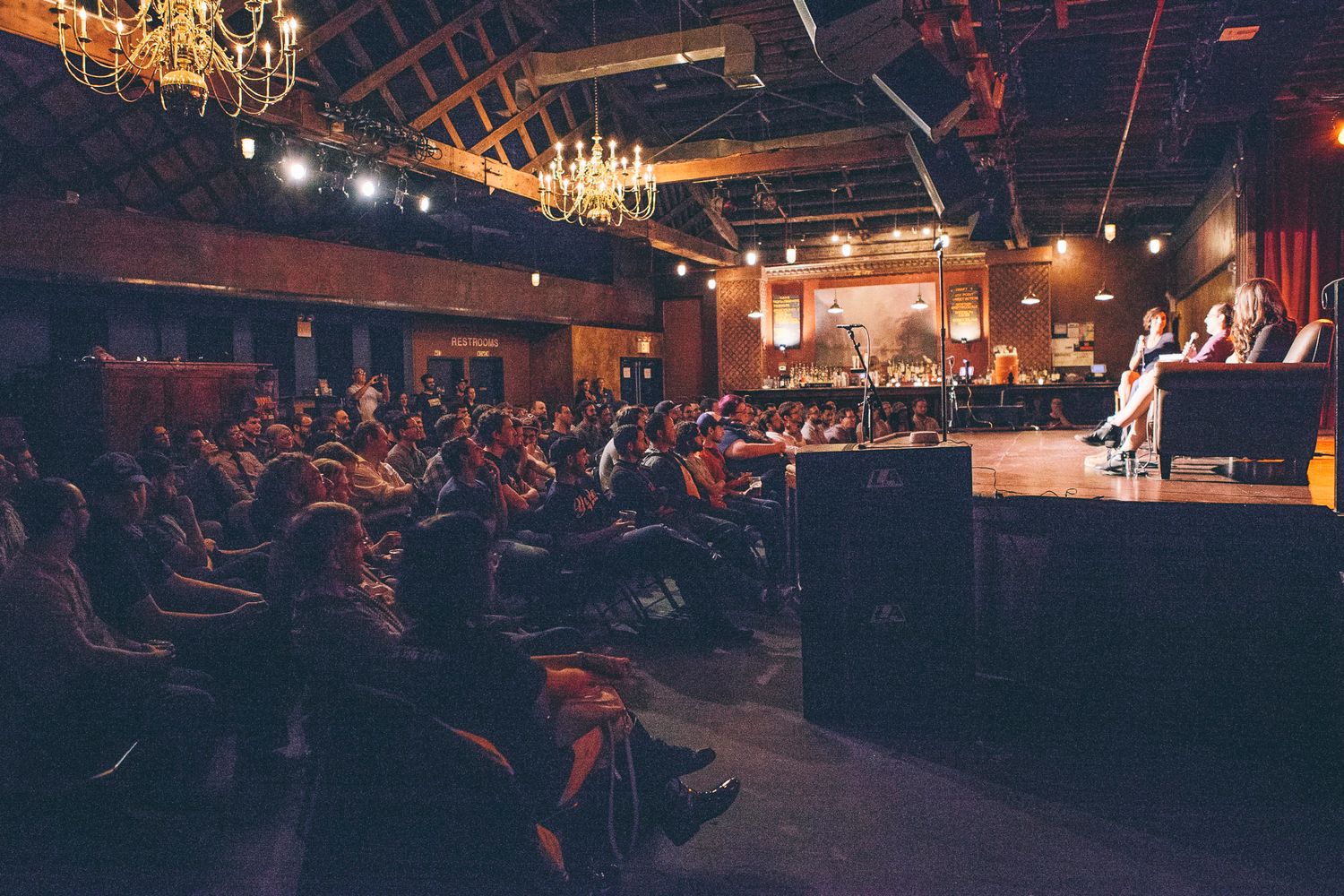 Large audience watching a panel discussion on a warmly lit stage in an elegant venue.