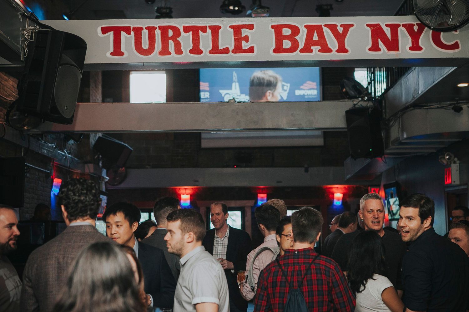Busy Turtle Bay NYC bar scene with guests mingling under red neon signage.