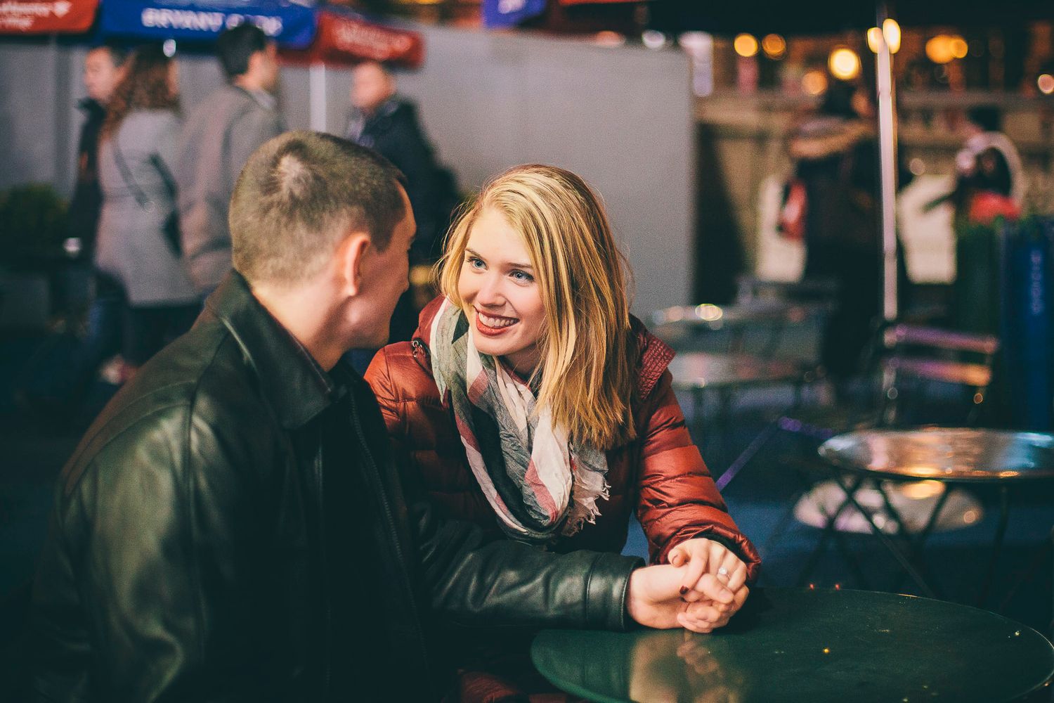 Young couple holding hands at outdoor cafe with festive lights at night.