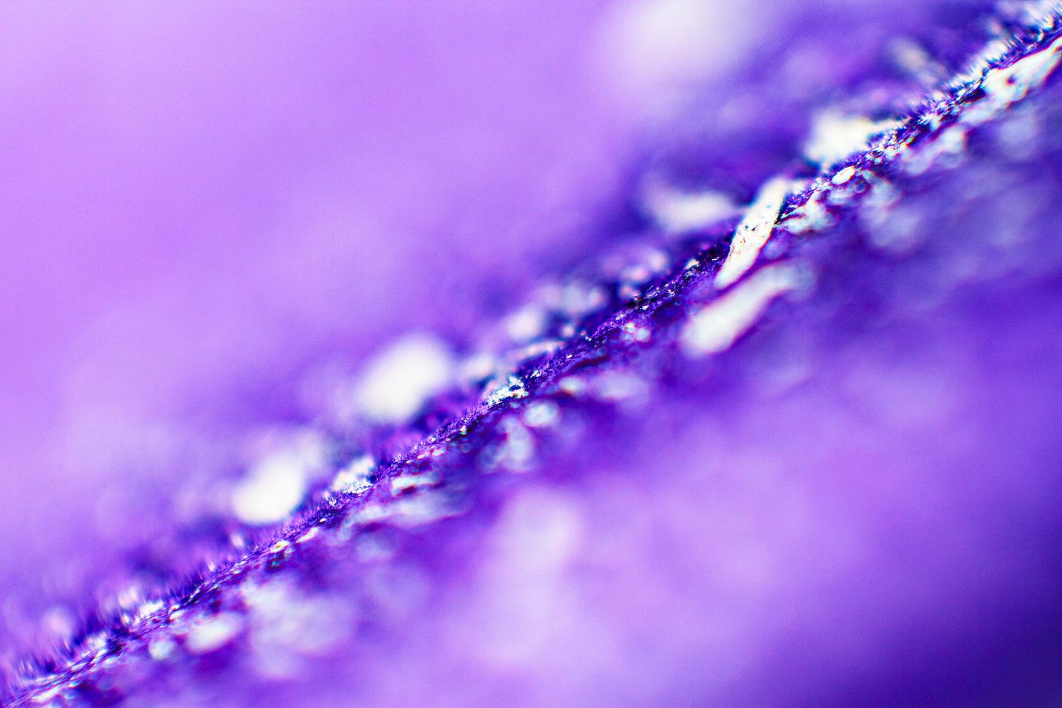 Close-up macro photograph of purple glittery fabric texture with shimmering silver threads and bokeh background.