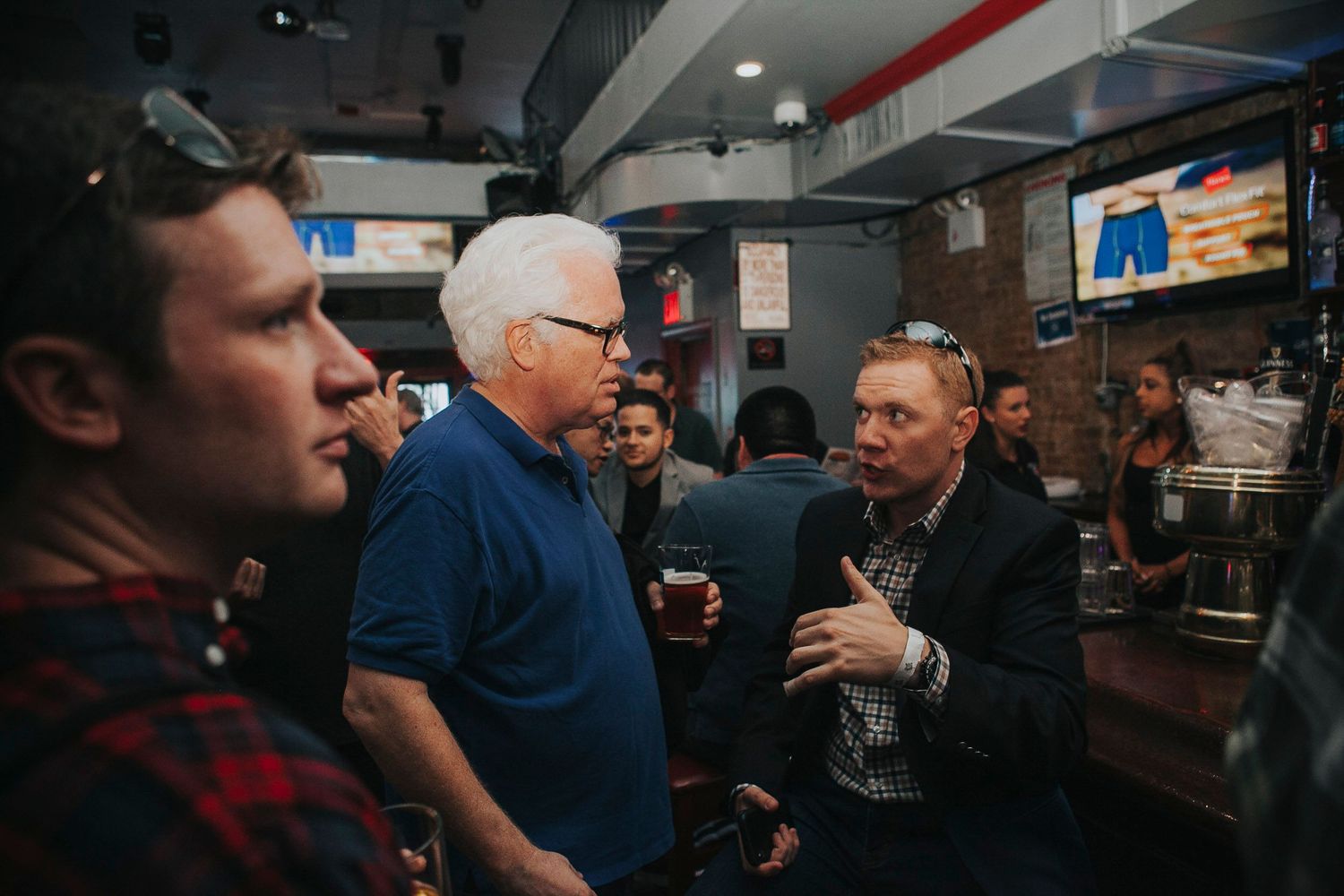 Group of men having a discussion at a crowded bar during an evening social event.