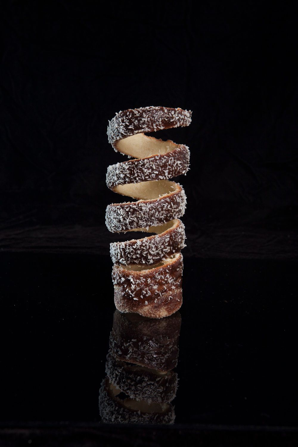 Stack of sliced coconut chocolate cookies balanced in a tower on black surface.