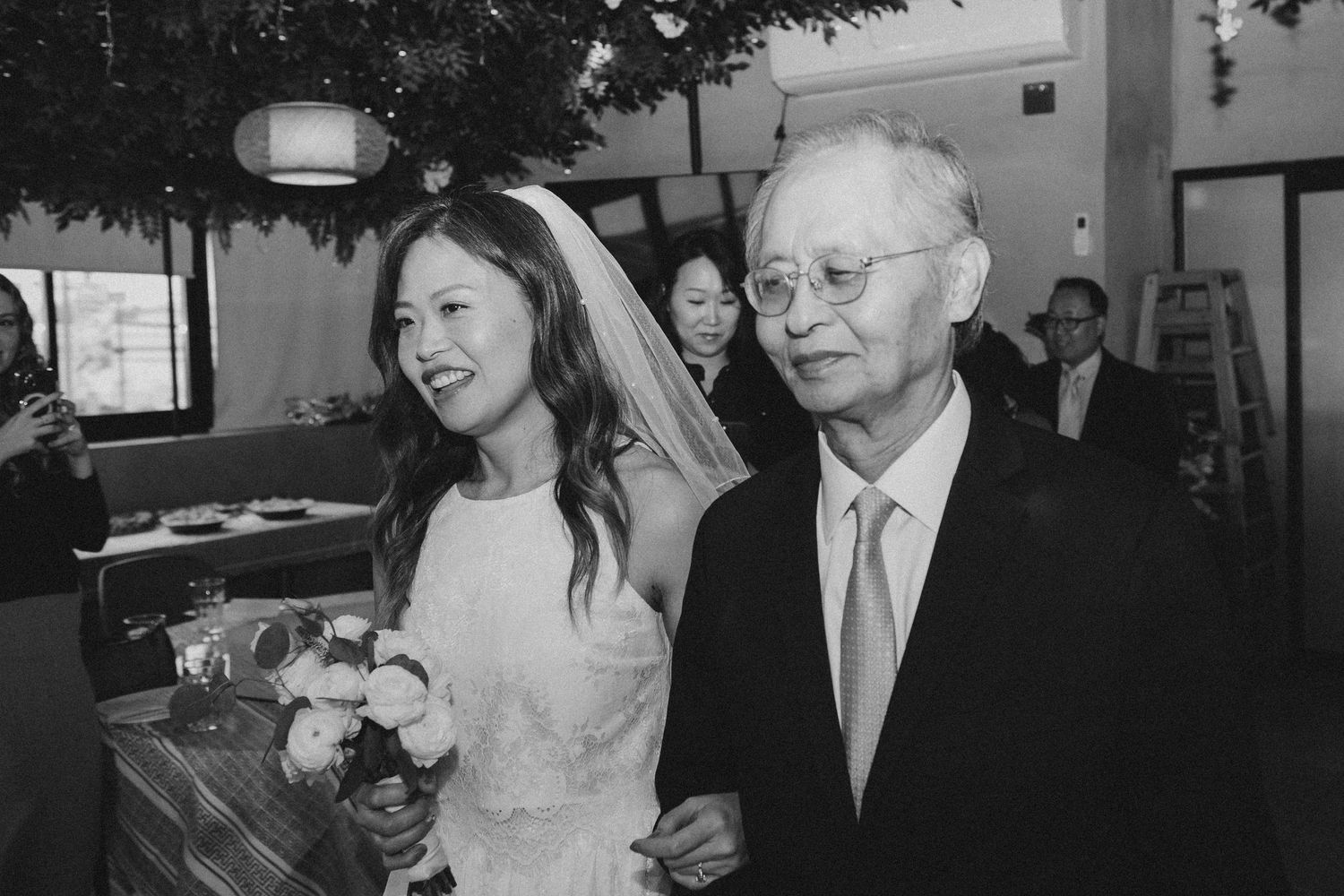Smiling bride walks down the aisle with her father during wedding ceremony procession.