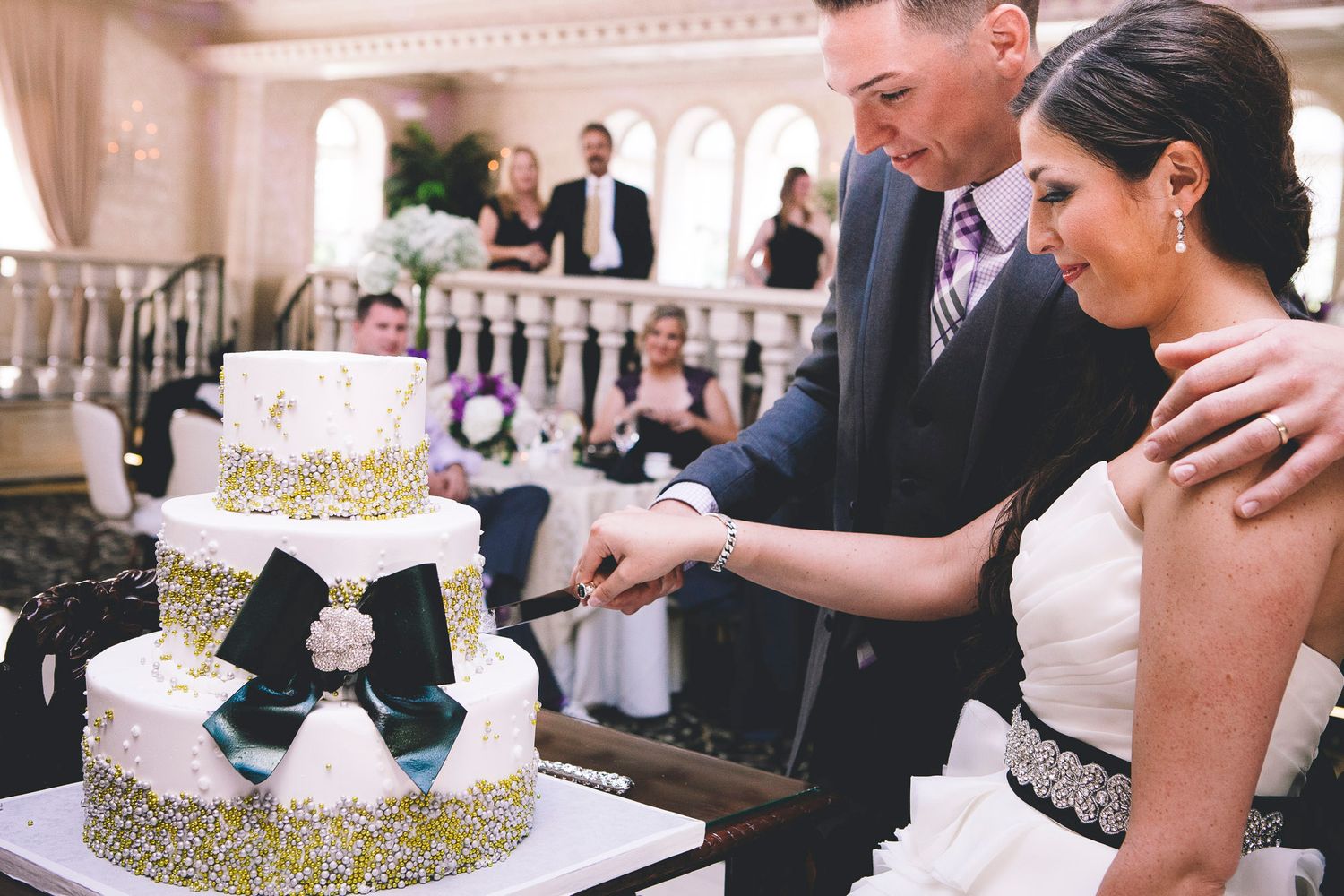 Bride and groom cutting their elegant three-tiered white and gold wedding cake at their reception.
