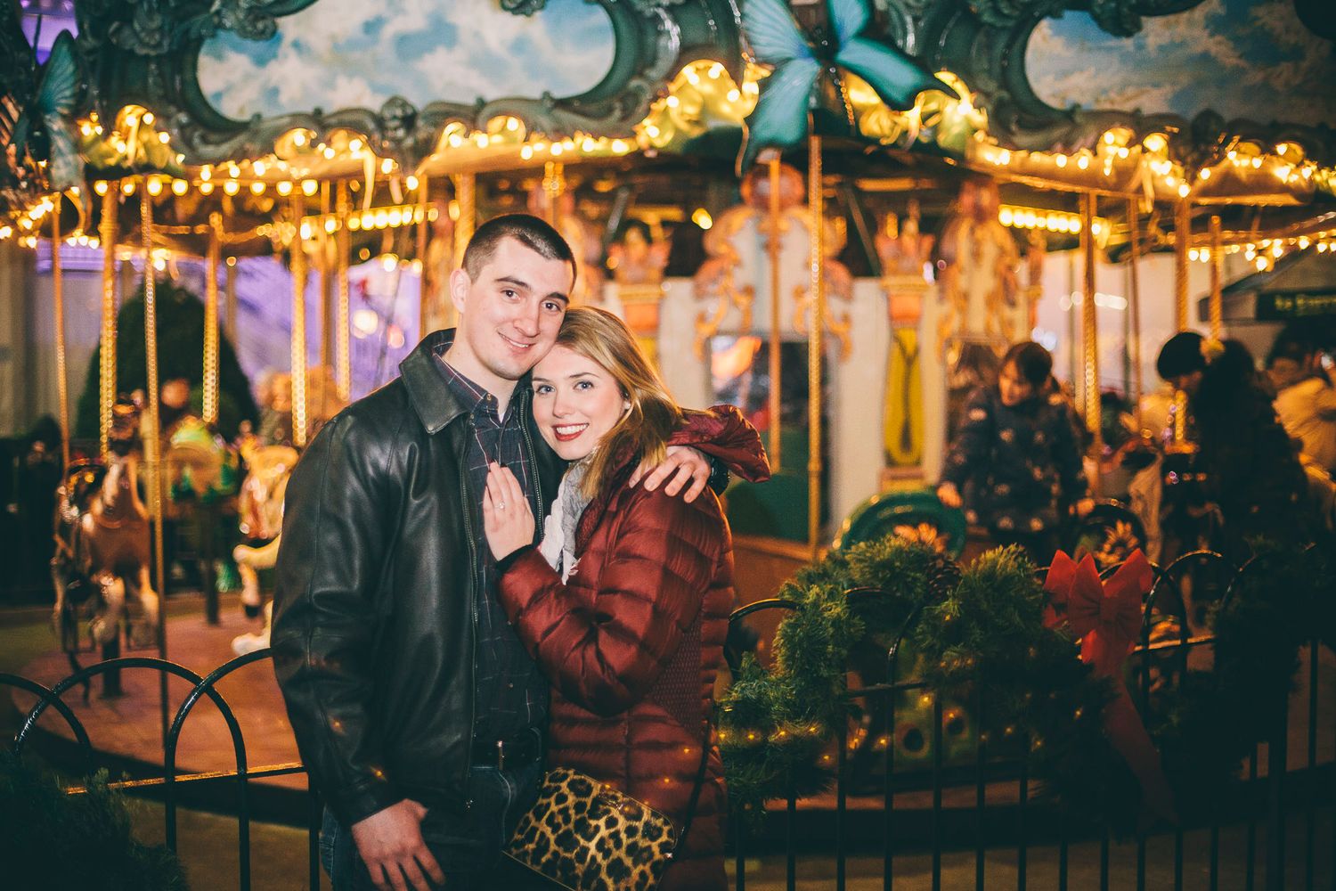 Romantic couple embracing in front of illuminated carousel at night fair.