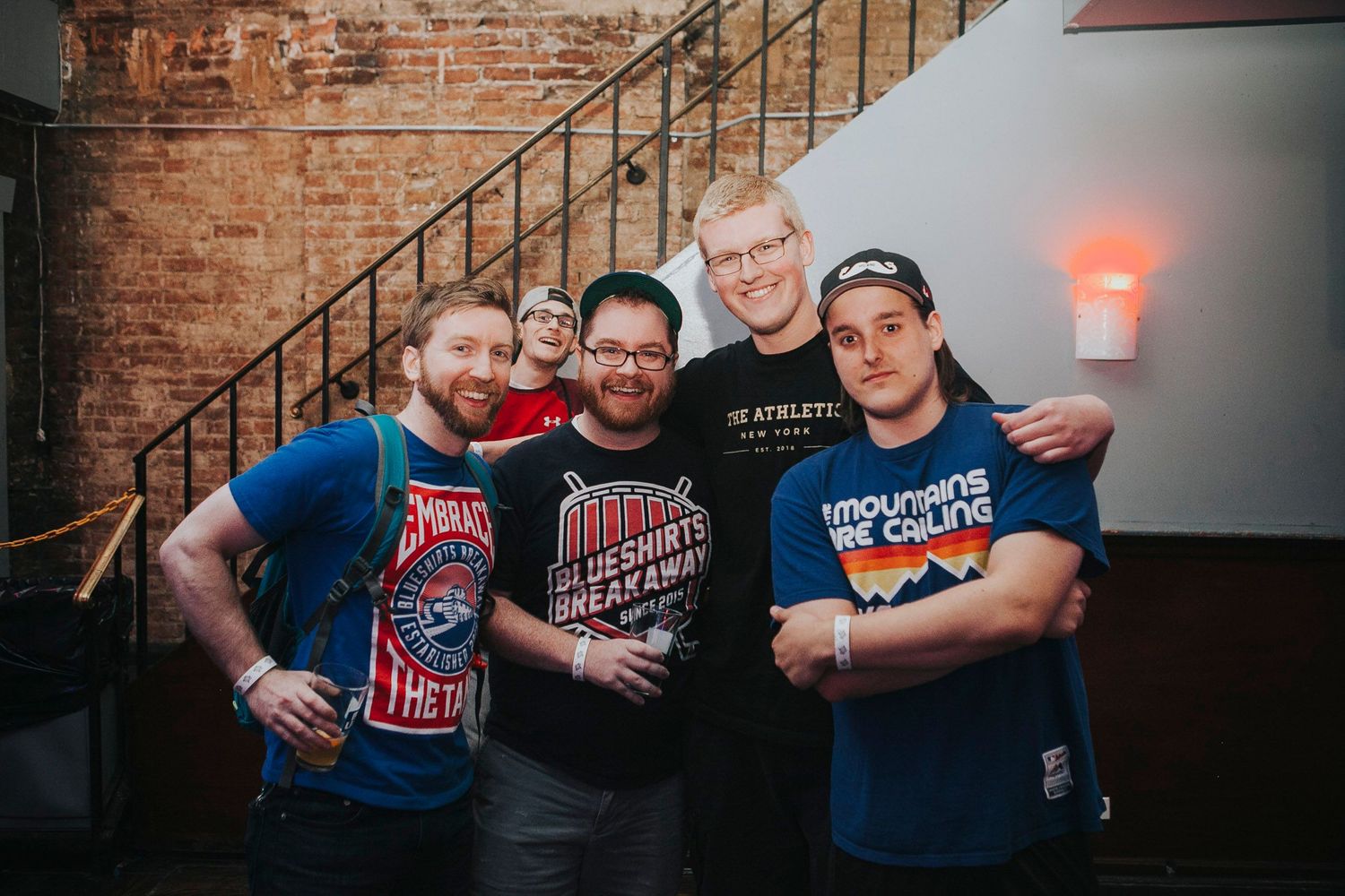 Four smiling men posing together for a group photo in a brick-walled venue.