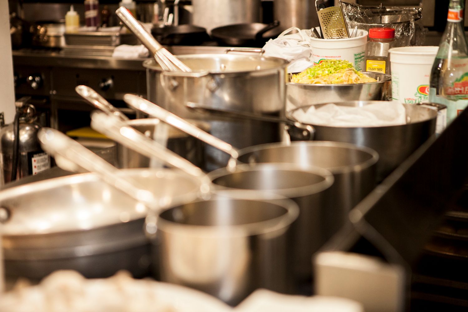 Rows of stainless steel pots and pans lined up on a professional restaurant kitchen counter.