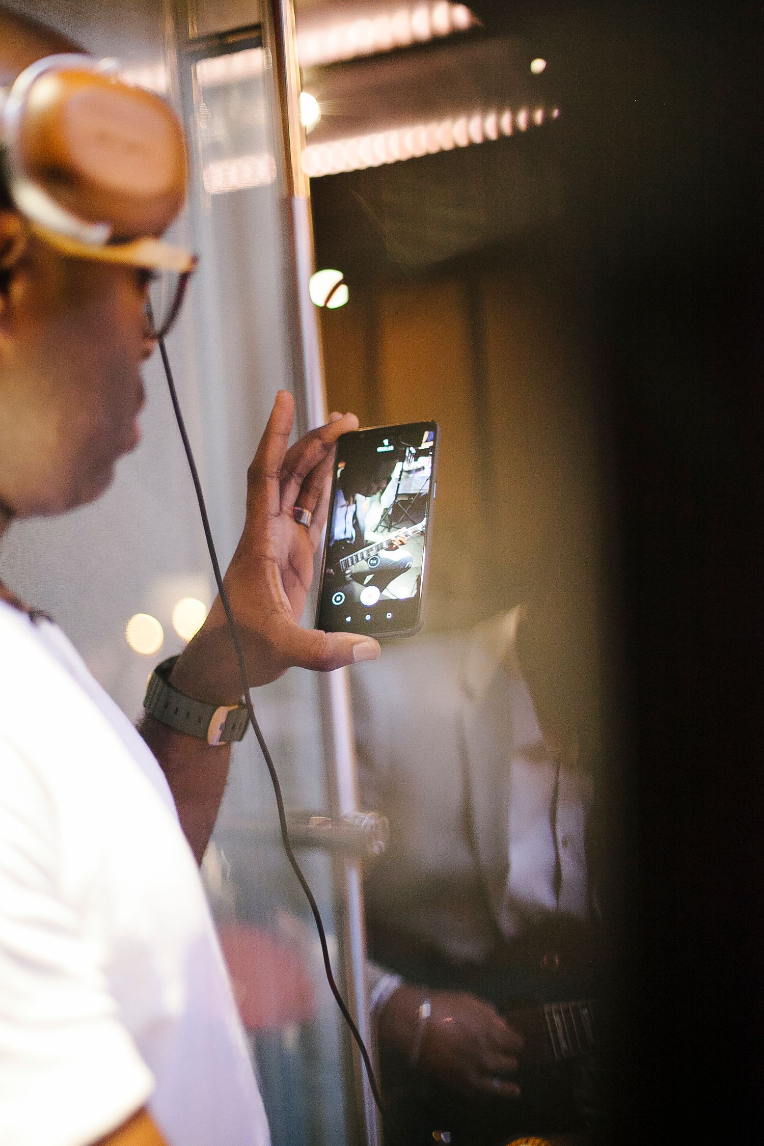 Man with headphones filming guitarist on smartphone at live music event.