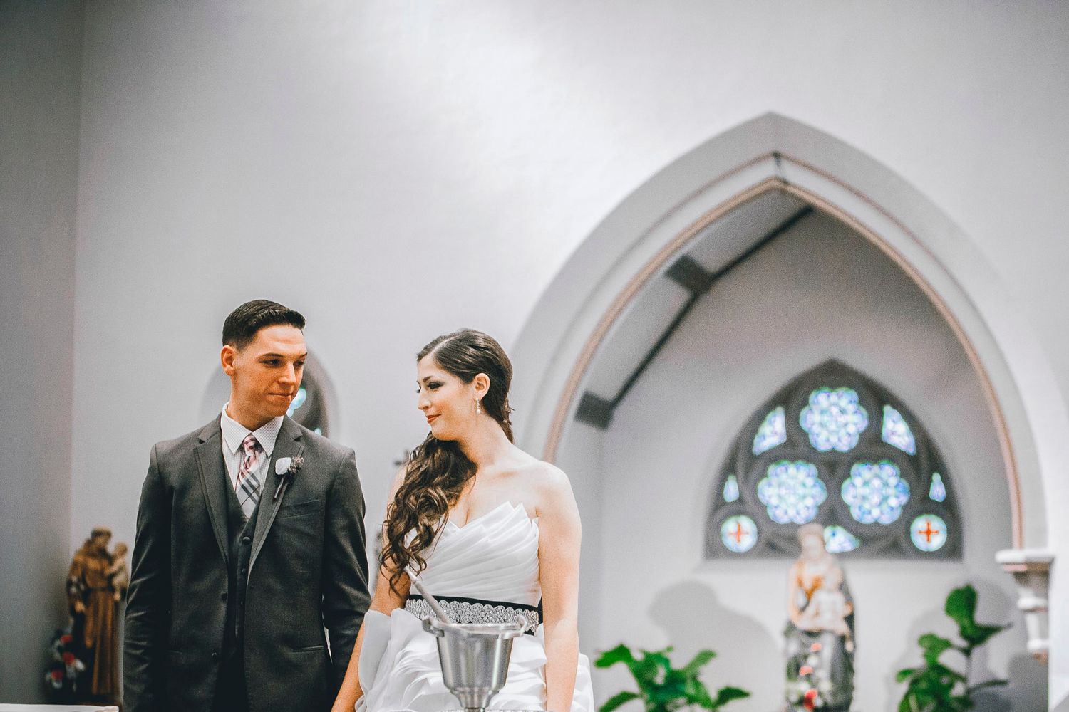 Bride and groom stand together inside a church with arched windows during their wedding ceremony.