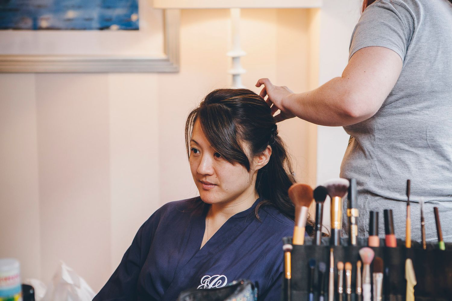 Asian bride getting hair styled by hairstylist while sitting in front of makeup brushes.