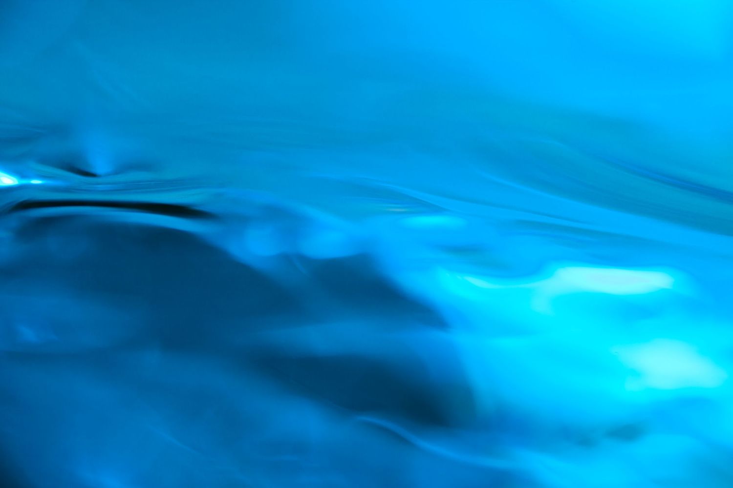 Abstract blue water surface with soft ripples and glowing light reflections creating a serene, fluid background.