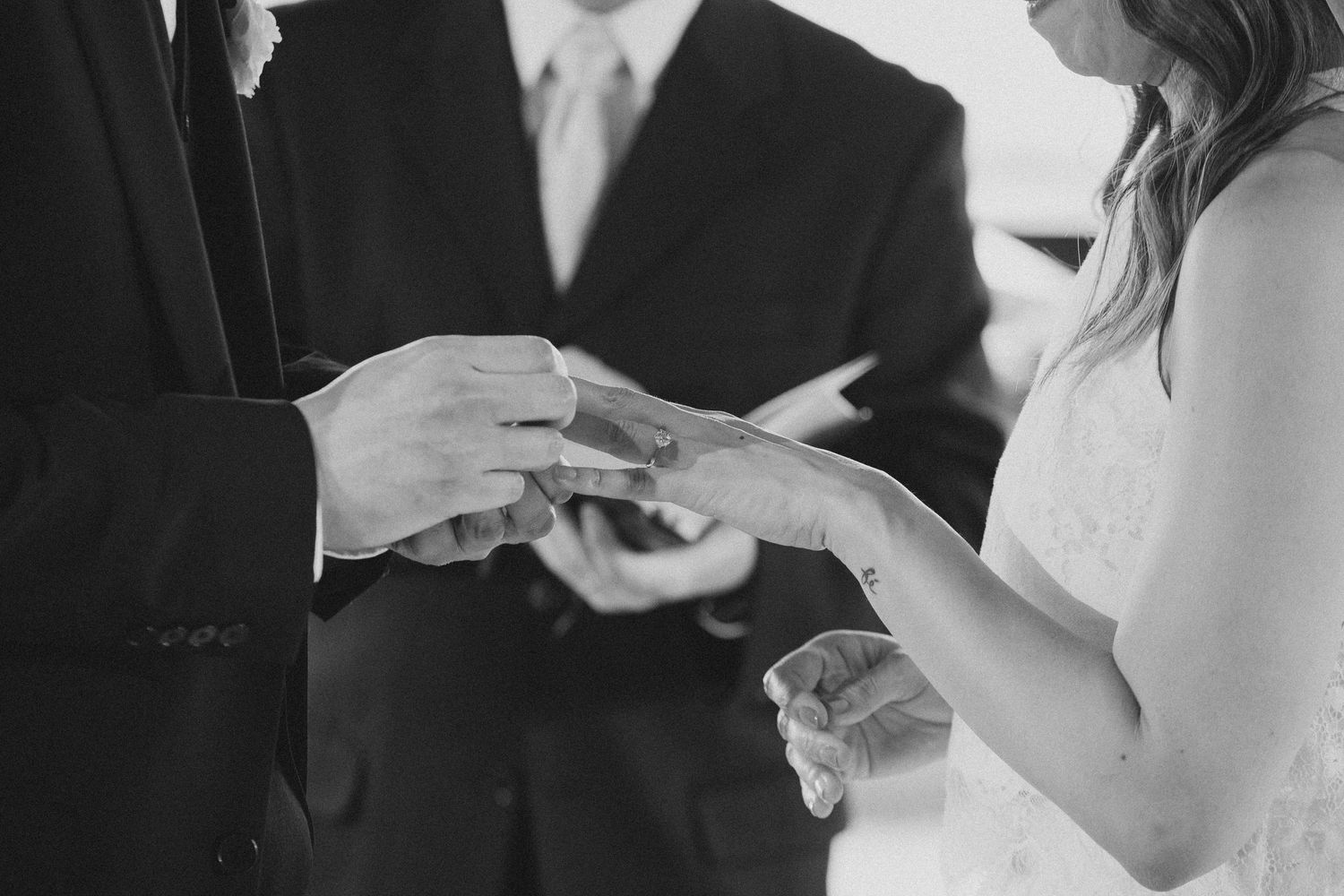 Bride and groom exchanging wedding rings during ceremony in black and white photo.