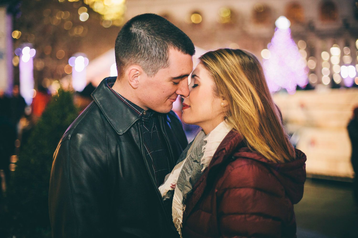 Romantic couple about to kiss with festive night lights in background.