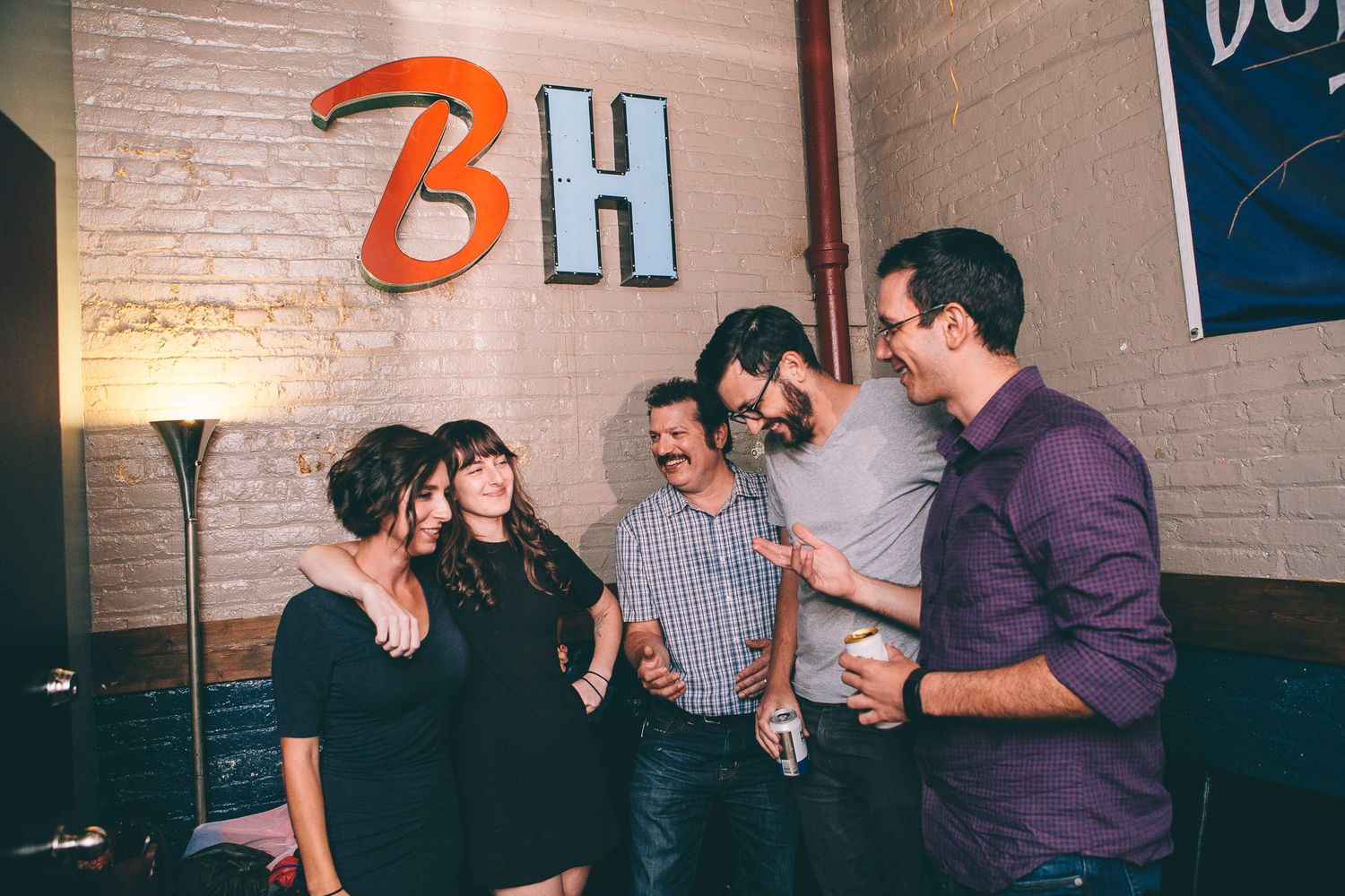 Group of five friends laughing and socializing at a casual indoor venue with brick walls.