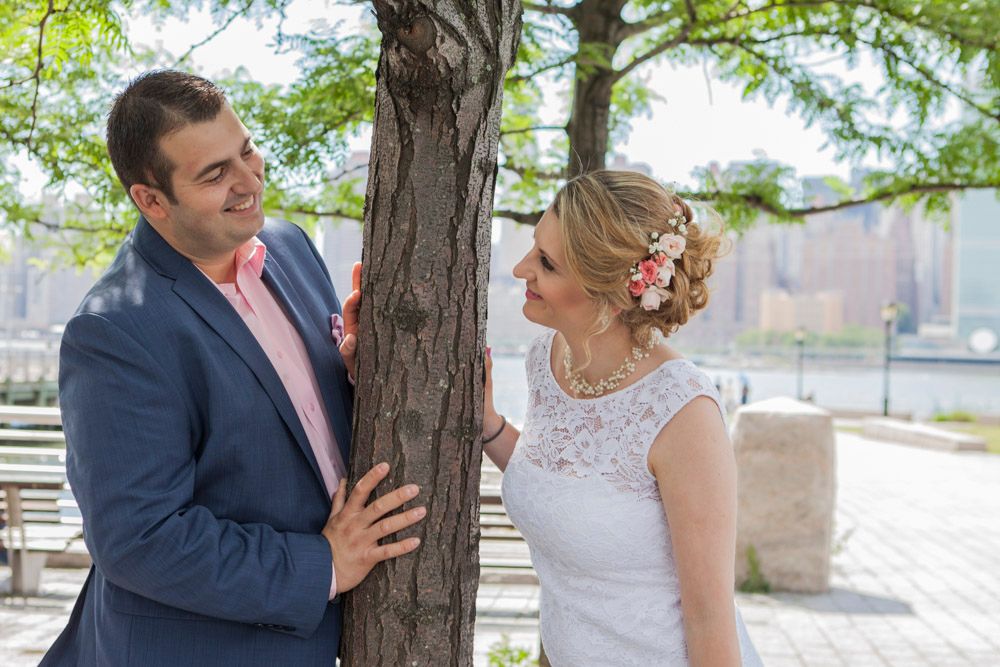 Bride and groom share a romantic moment by a tree with NYC skyline in background on their wedding day.