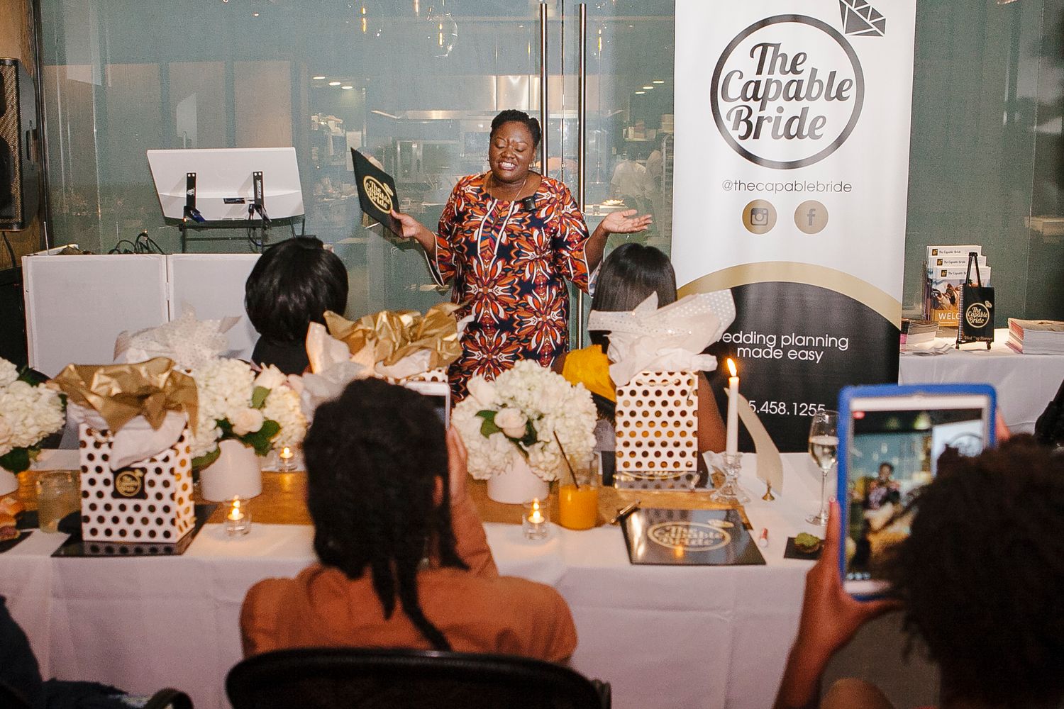 Woman presenting at The Capable Bride wedding planning event surrounded by floral arrangements and gift bags.