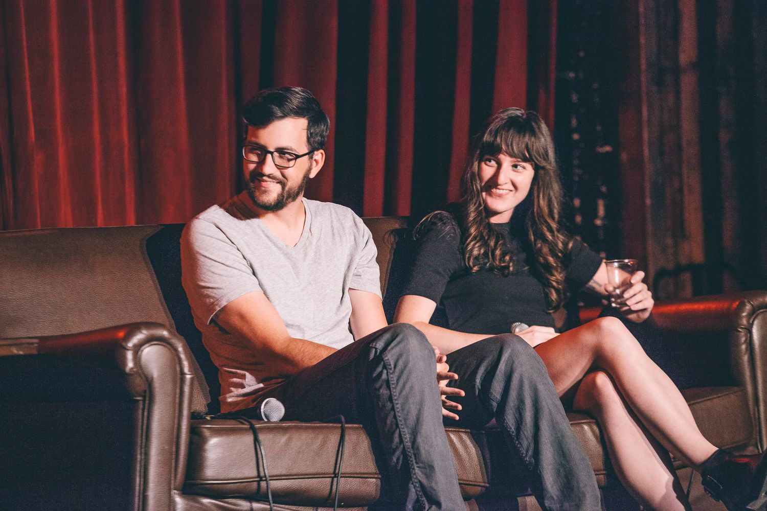 Man and woman smiling together on leather couch during on-stage panel discussion.