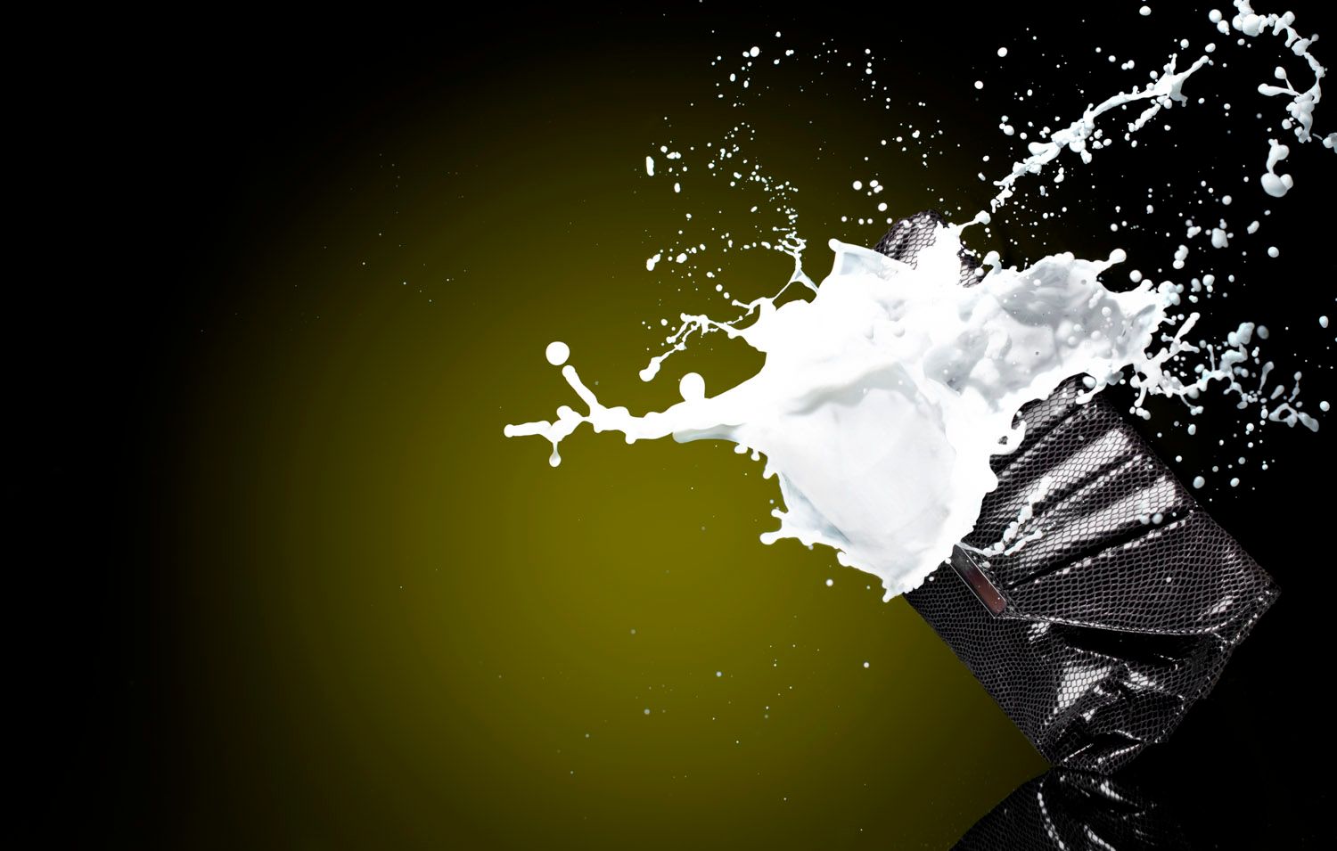 Dynamic splash of white milk bursting from black and white packaging against an olive green background.