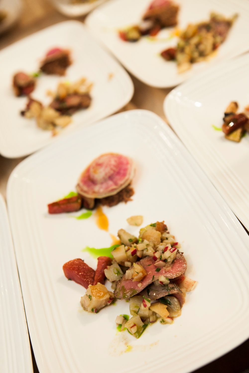Elegant plated beef dish with watermelon radish, mushrooms, and colorful garnishes on white plates.