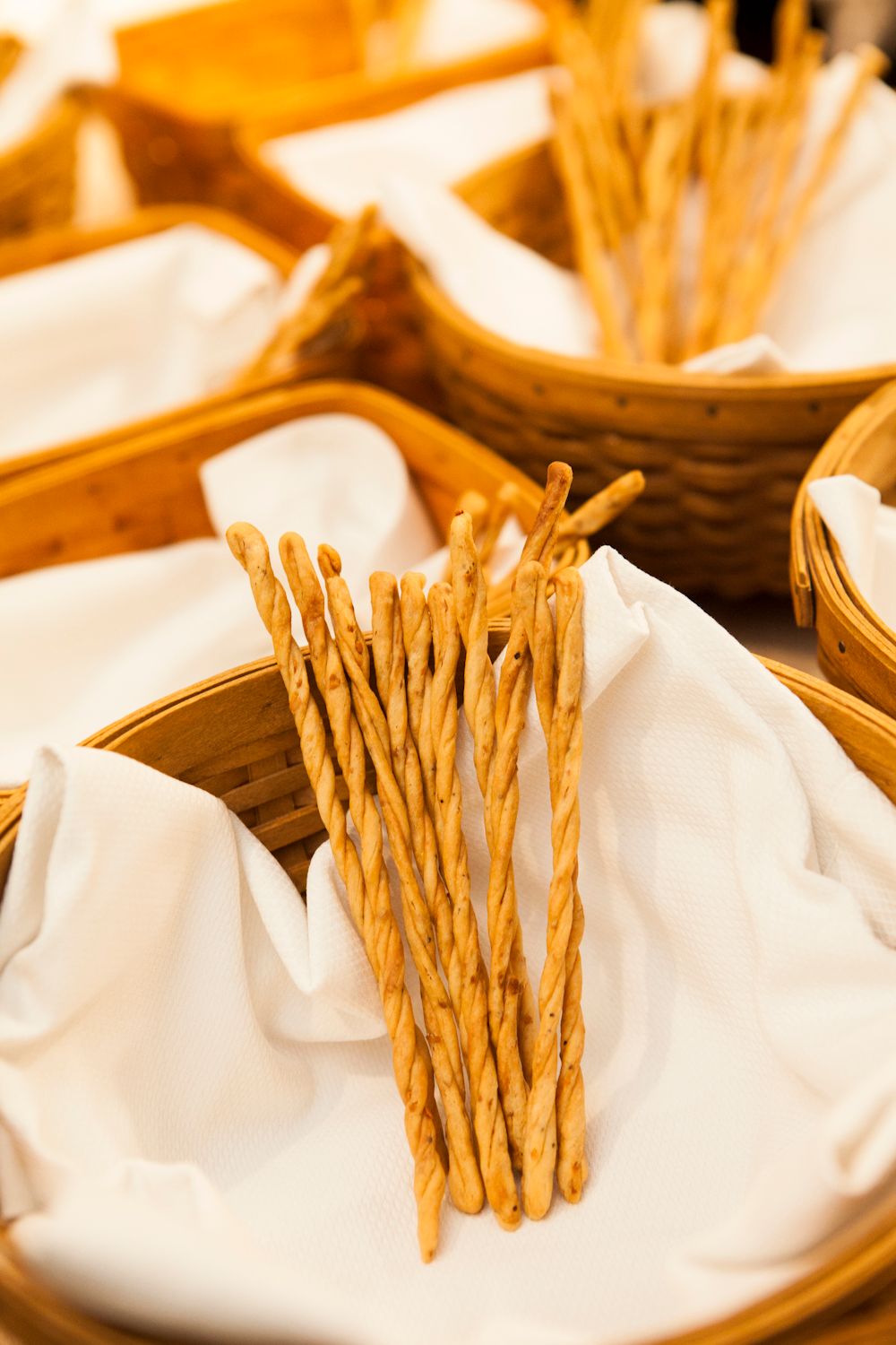 Crispy twisted breadsticks standing upright in wicker baskets lined with white napkins.