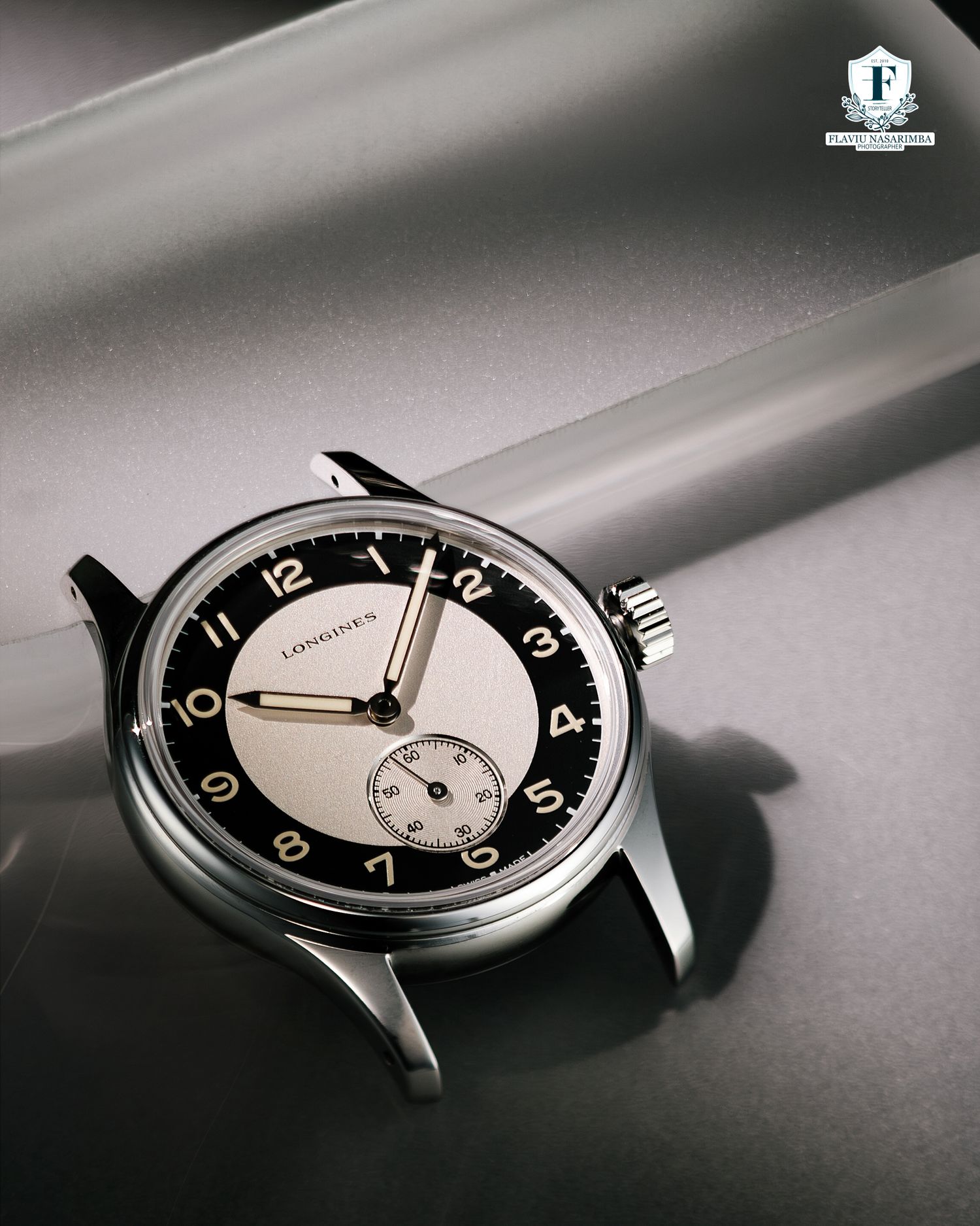 Longines Heritage Classic stainless steel watch with two-tone black and silver dial on gray surface.