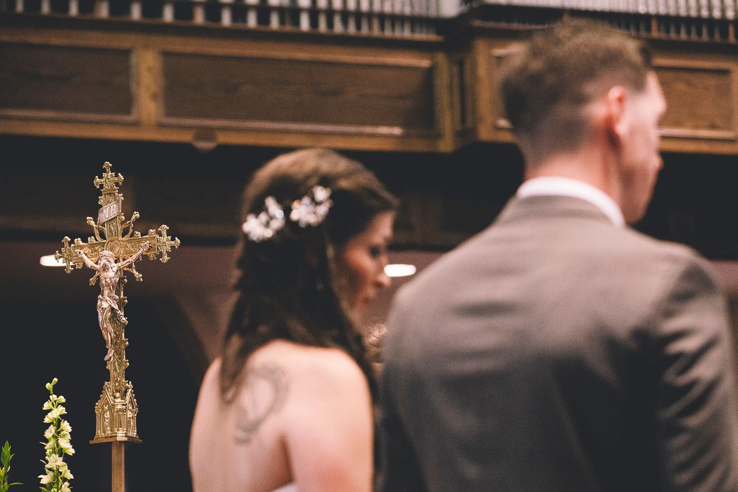 Bride with floral hair accessory and groom stand near golden crucifix during church wedding ceremony.
