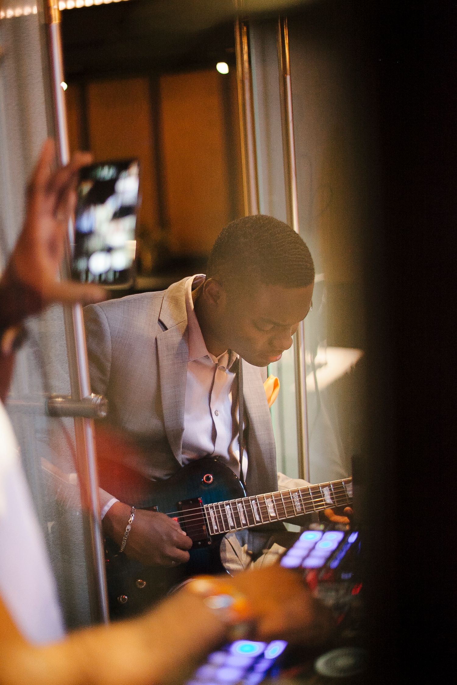Young musician in gray suit playing electric guitar at an indoor event.