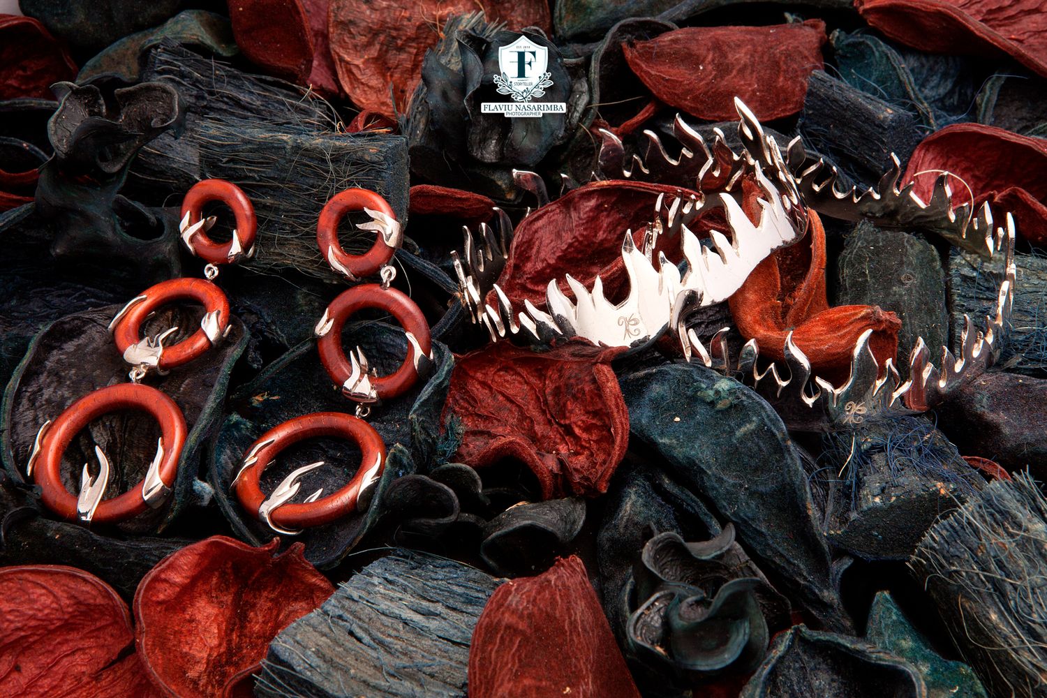 Bold red and black spike jewelry collection with hoop earrings displayed on dramatic dark foliage.