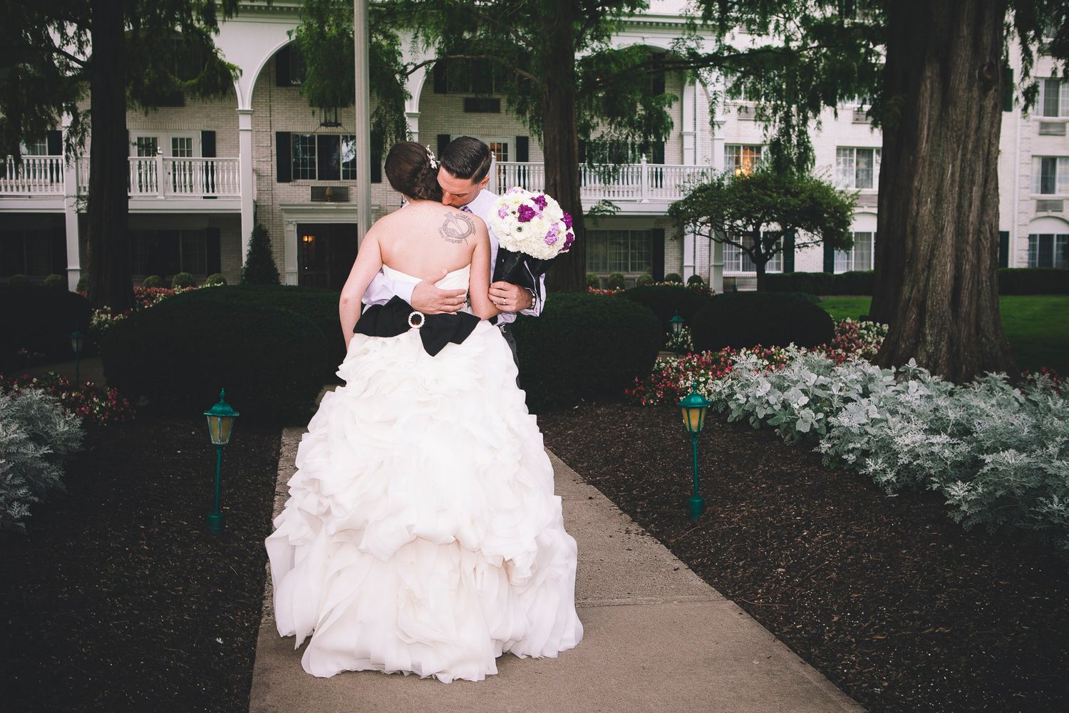 Bride in strapless ruffled gown with black sash walks away holding purple bridal bouquet.