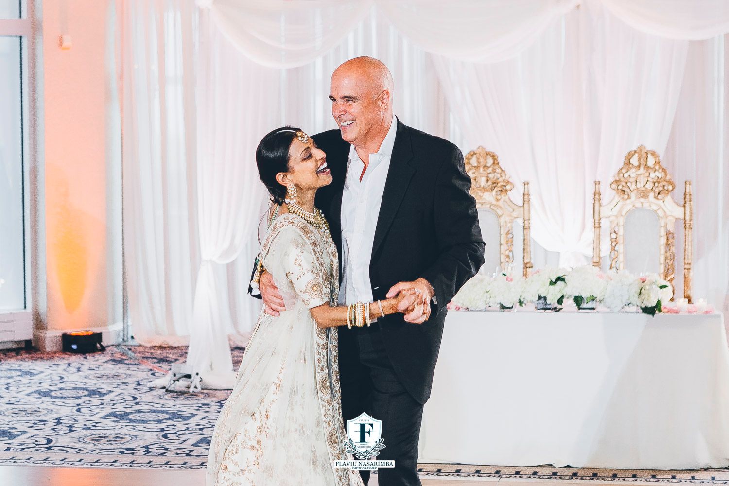 Bride in embroidered lehenga and groom in black suit share joyful first dance at Indian wedding reception.