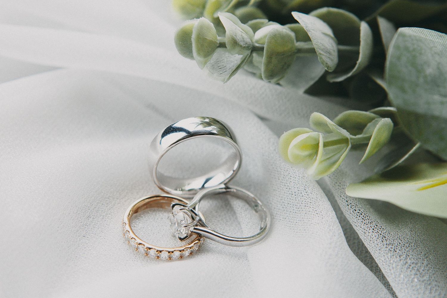 Three elegant wedding rings including diamond engagement ring and gold band arranged on white fabric.