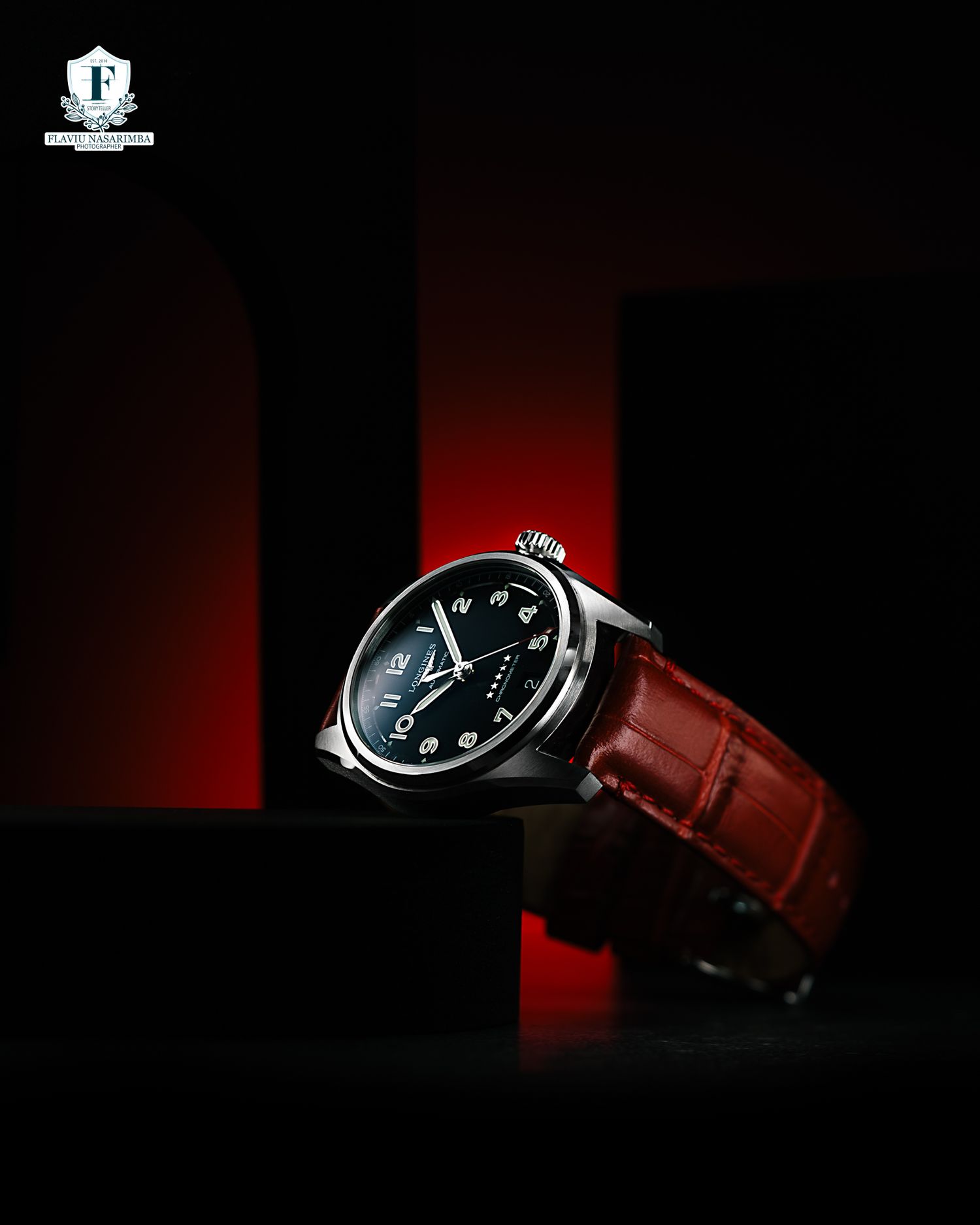 Classic dress watch with black dial and red alligator leather strap against dramatic red backdrop.