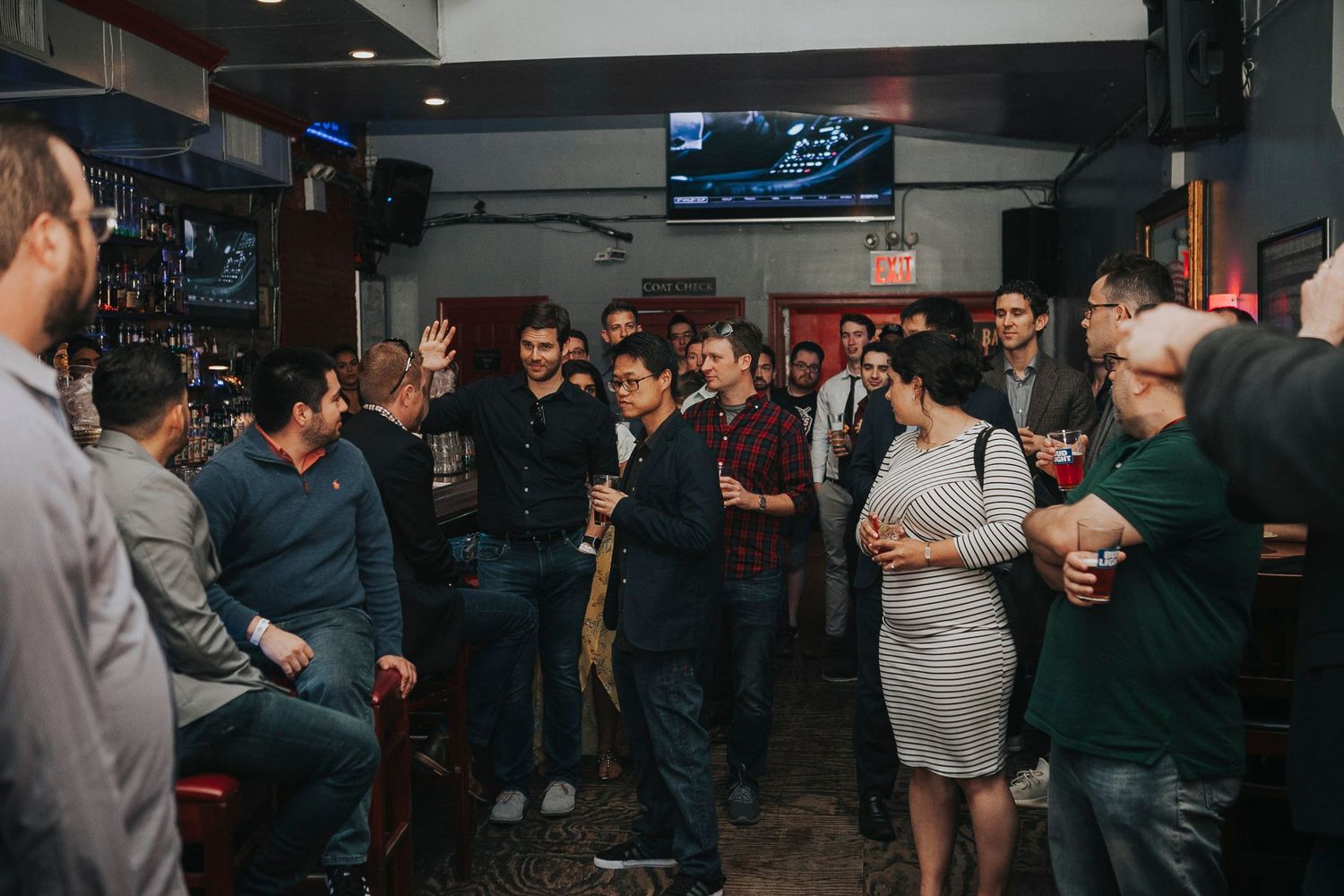 Large group of professionals networking and socializing at a busy bar gathering.
