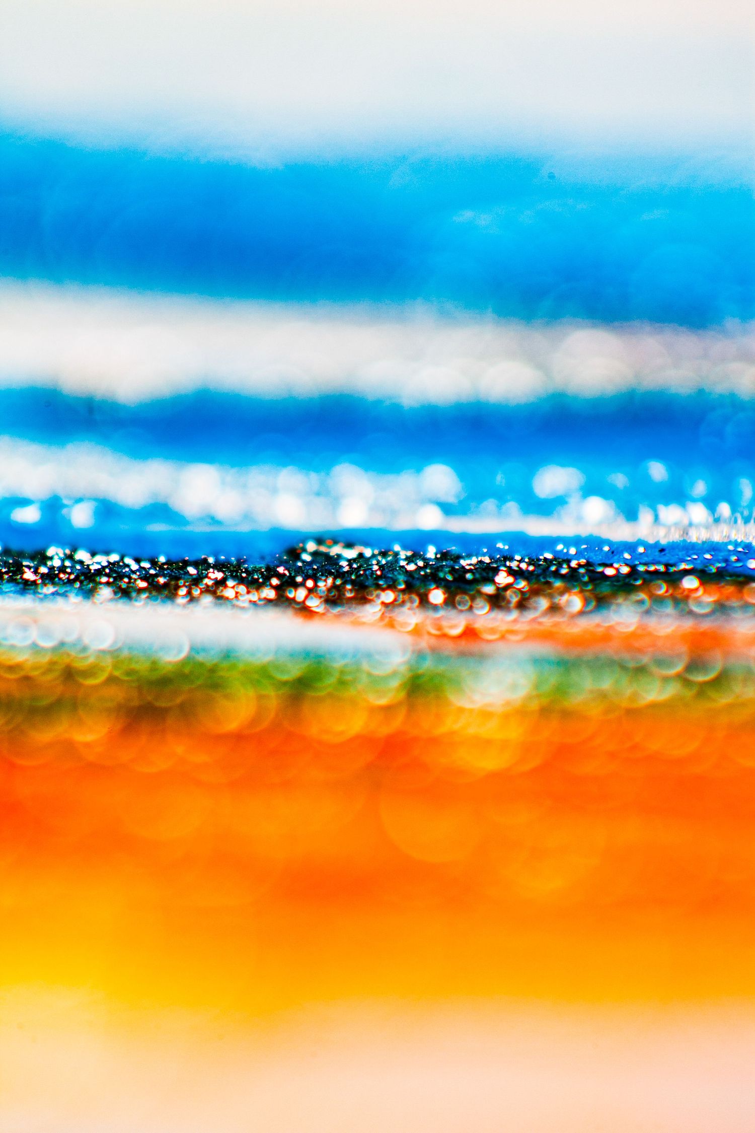Abstract bokeh art with vibrant blue, orange, and yellow horizontal bands creating a dreamy coastal landscape effect.