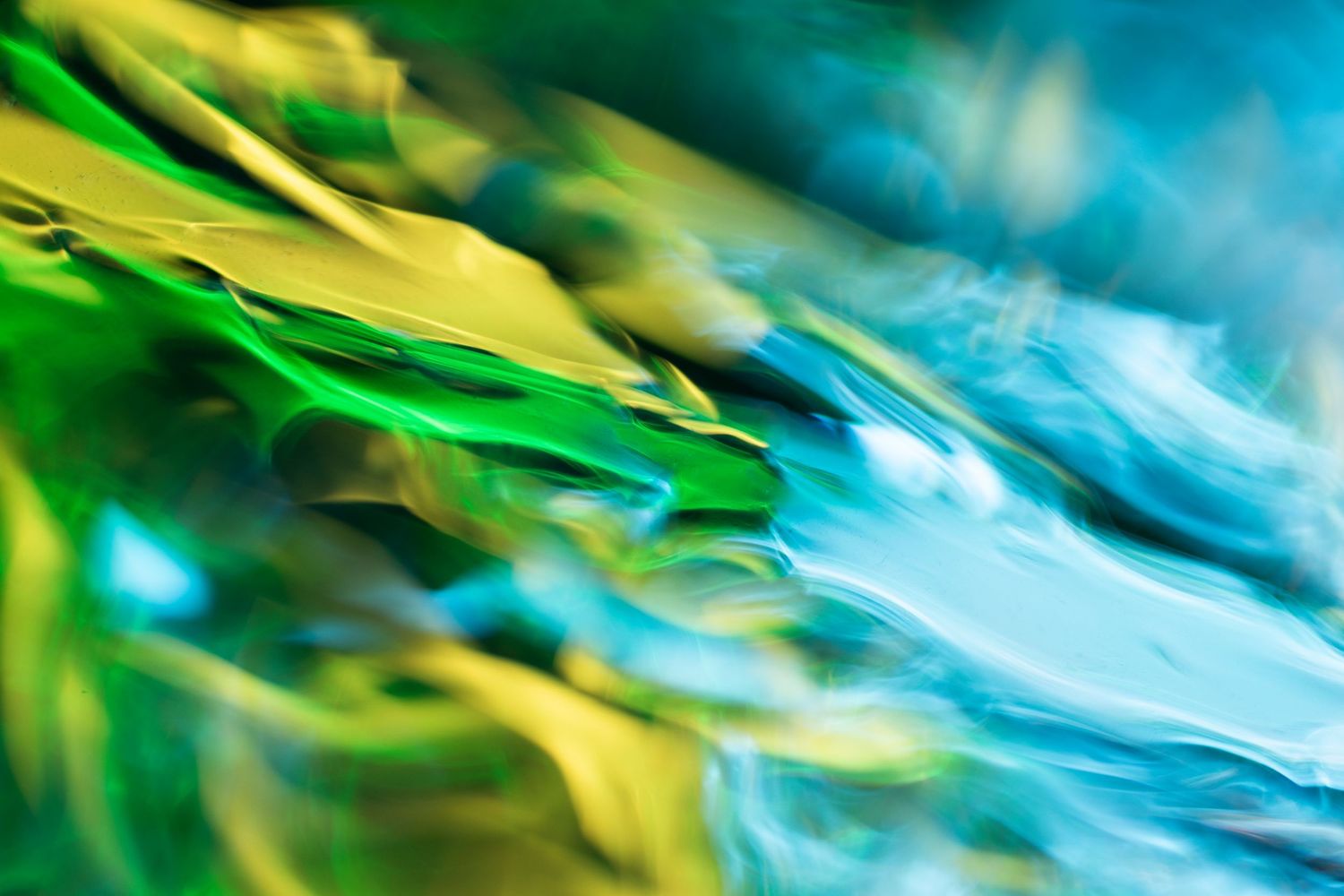 Abstract macro photography of vibrant green, yellow, and blue flowing liquid colors creating a dynamic wave pattern.