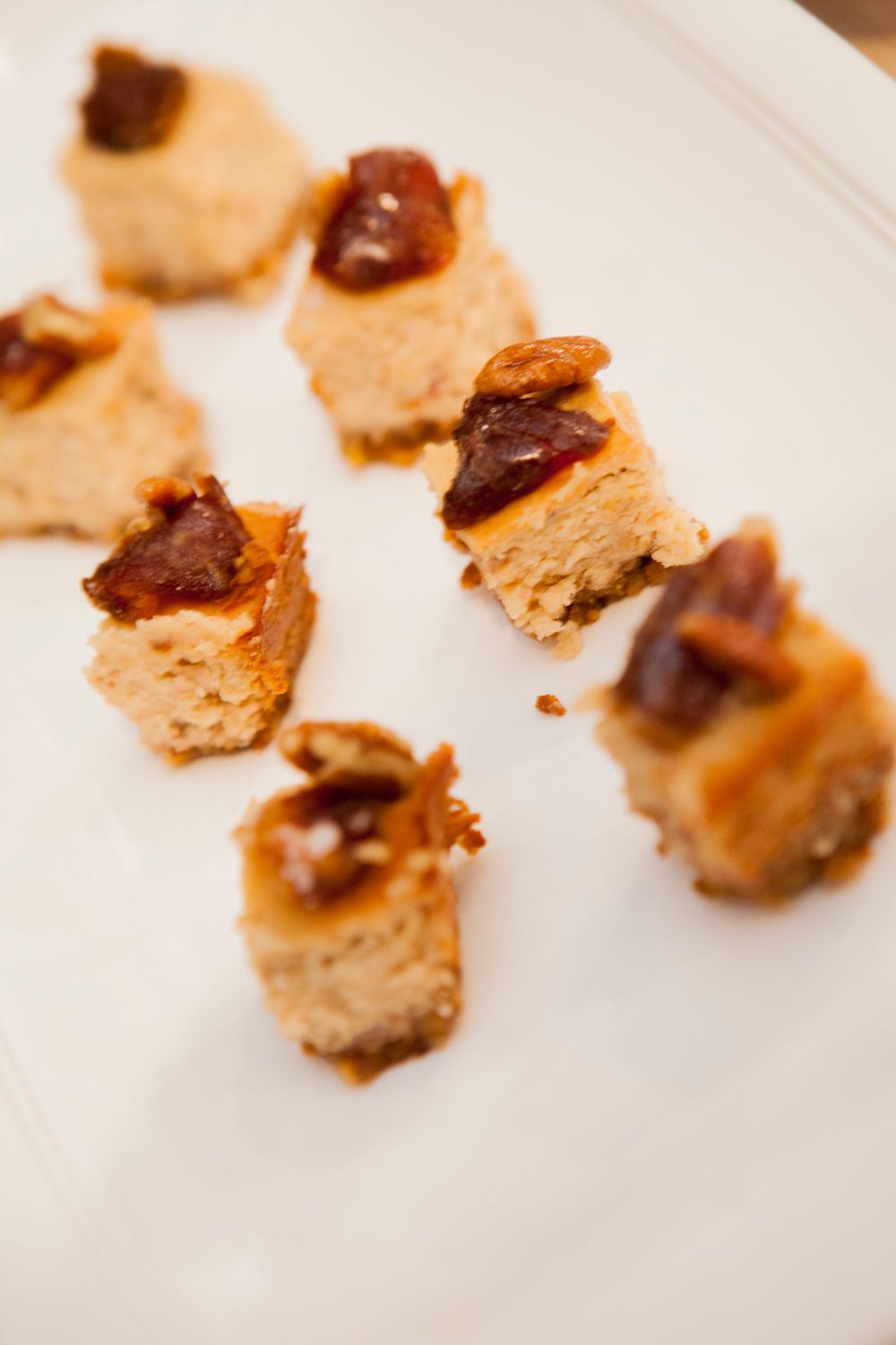 Small square foie gras or pate bites topped with caramelized fruit on a white serving plate.
