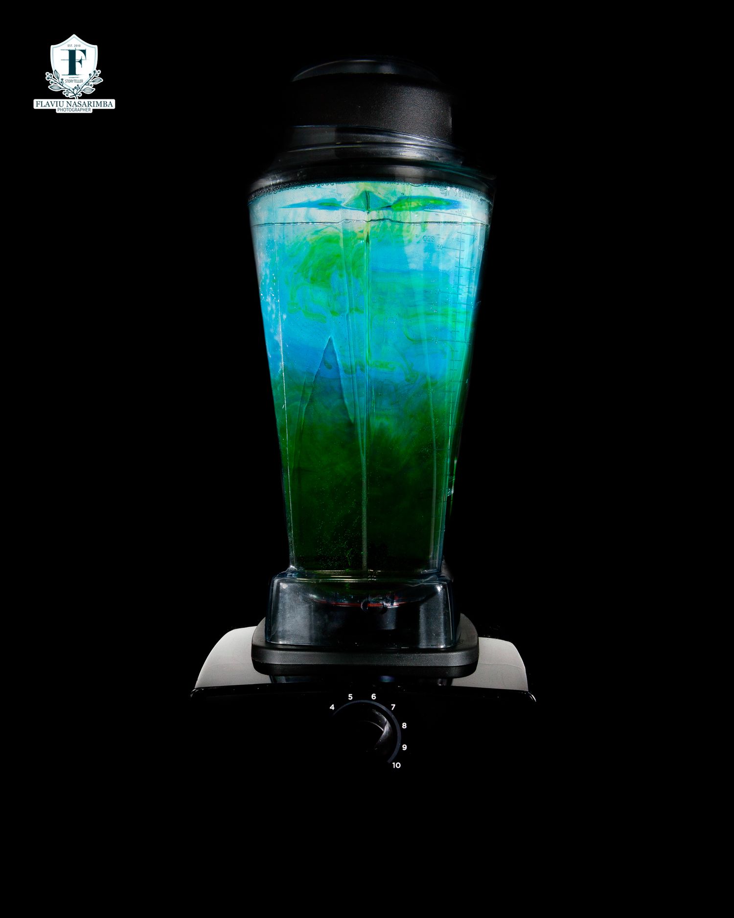 Electric blender with vibrant blue and green liquid mixture in clear pitcher on black background.