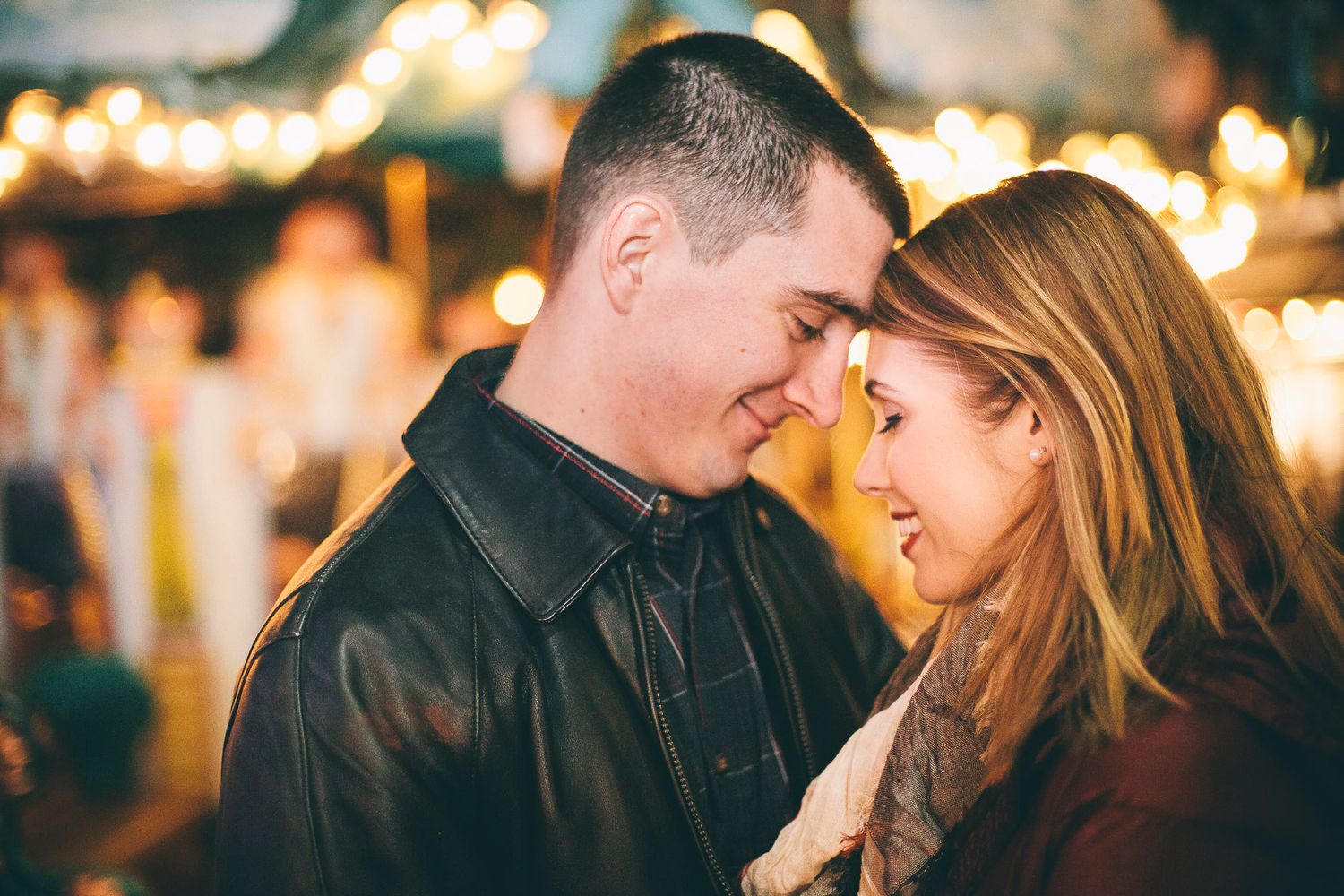 Loving couple touching foreheads and smiling in warm bokeh night lights.