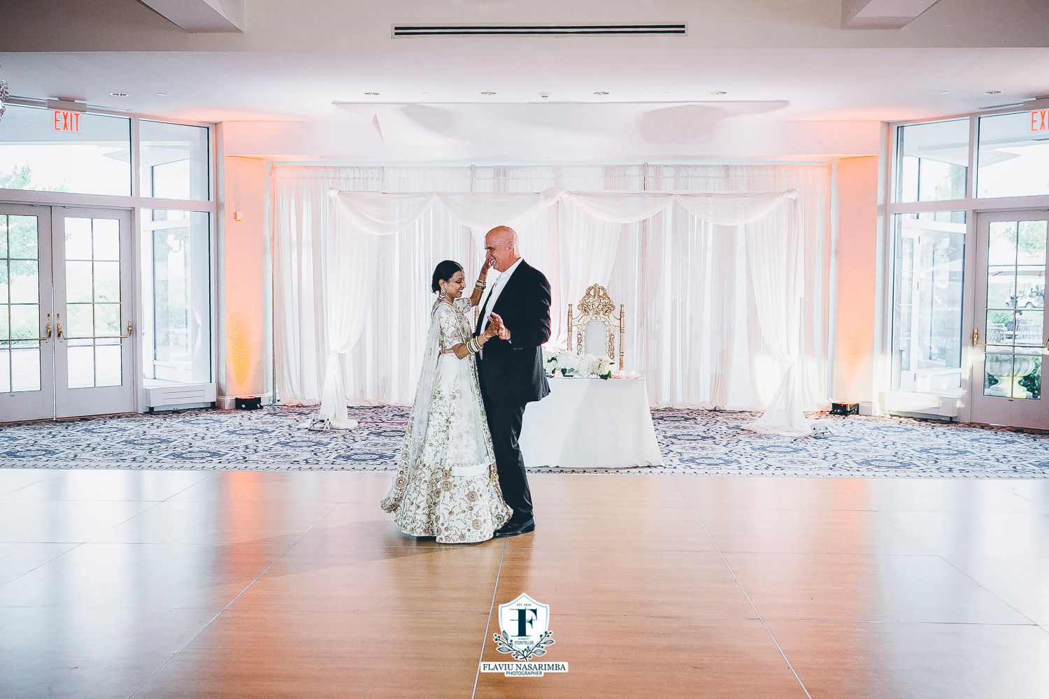 Couple shares romantic first dance in elegant white-draped ballroom during Indian wedding reception celebration.