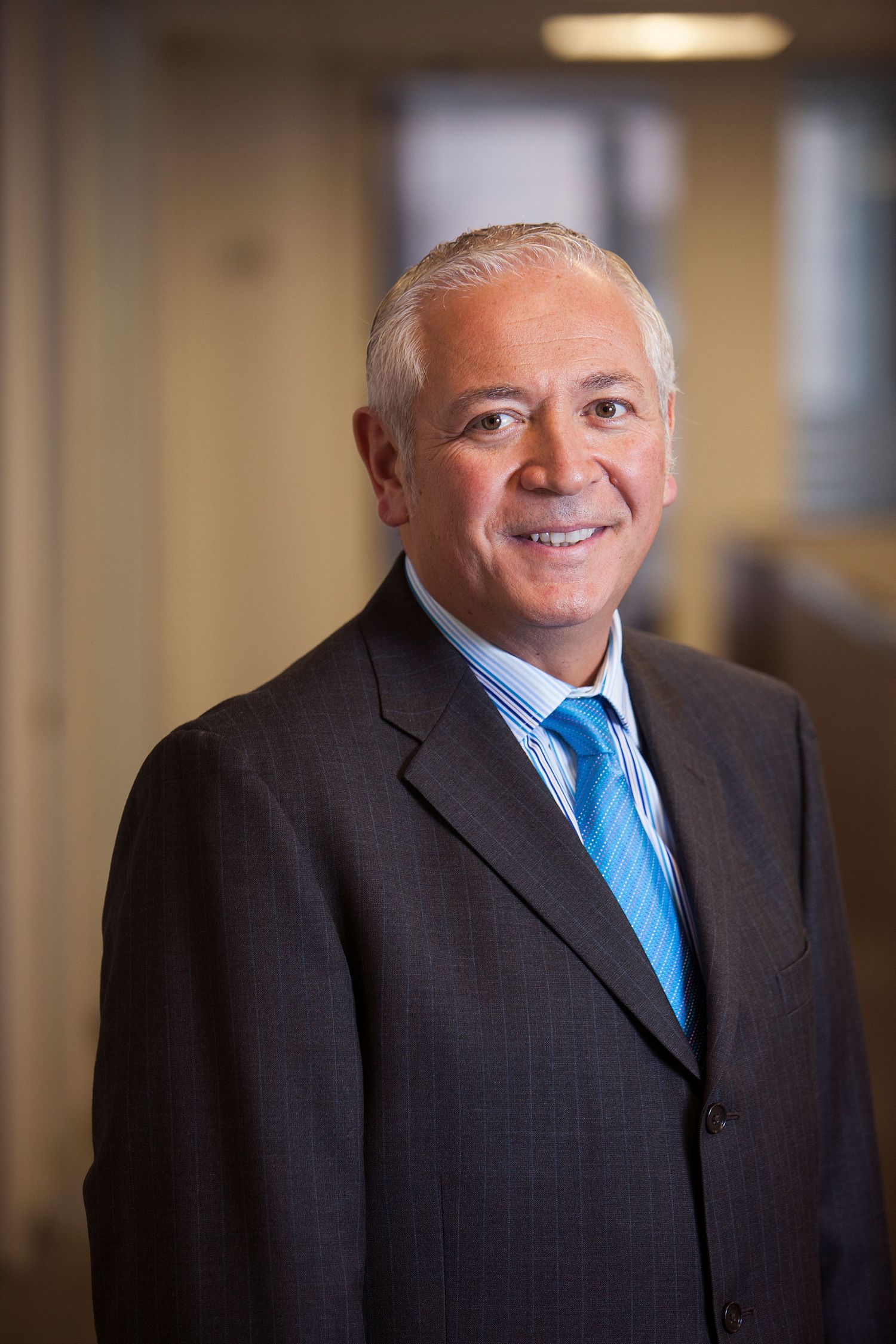 Professional headshot of smiling senior businessman with gray hair wearing dark suit and blue striped tie.